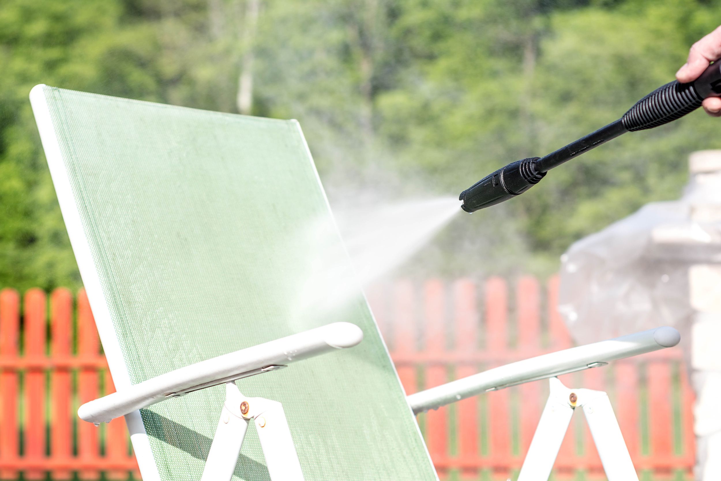 person with water sprayer cleaning garden furniture
