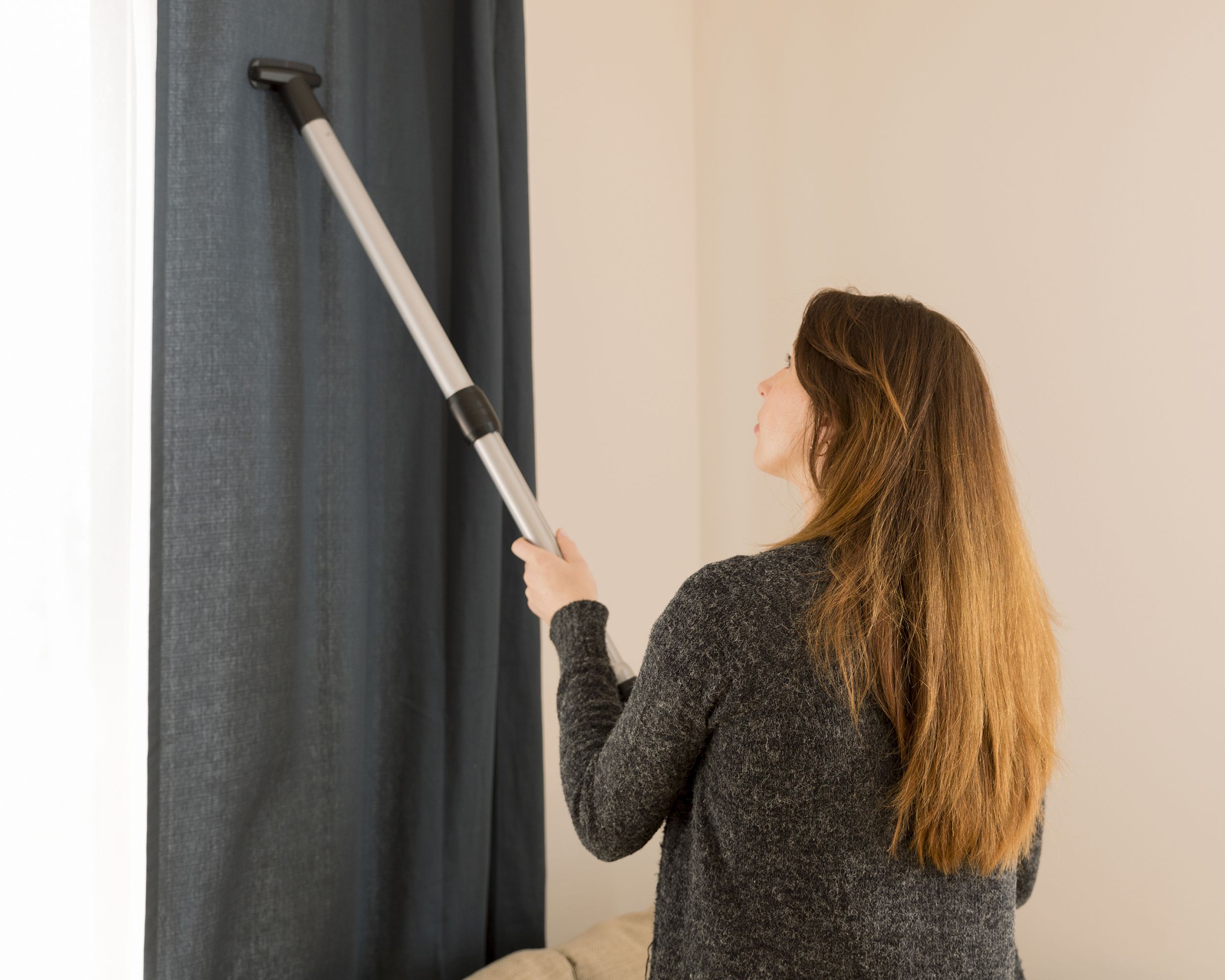 woman cleaning curtains with vacuum