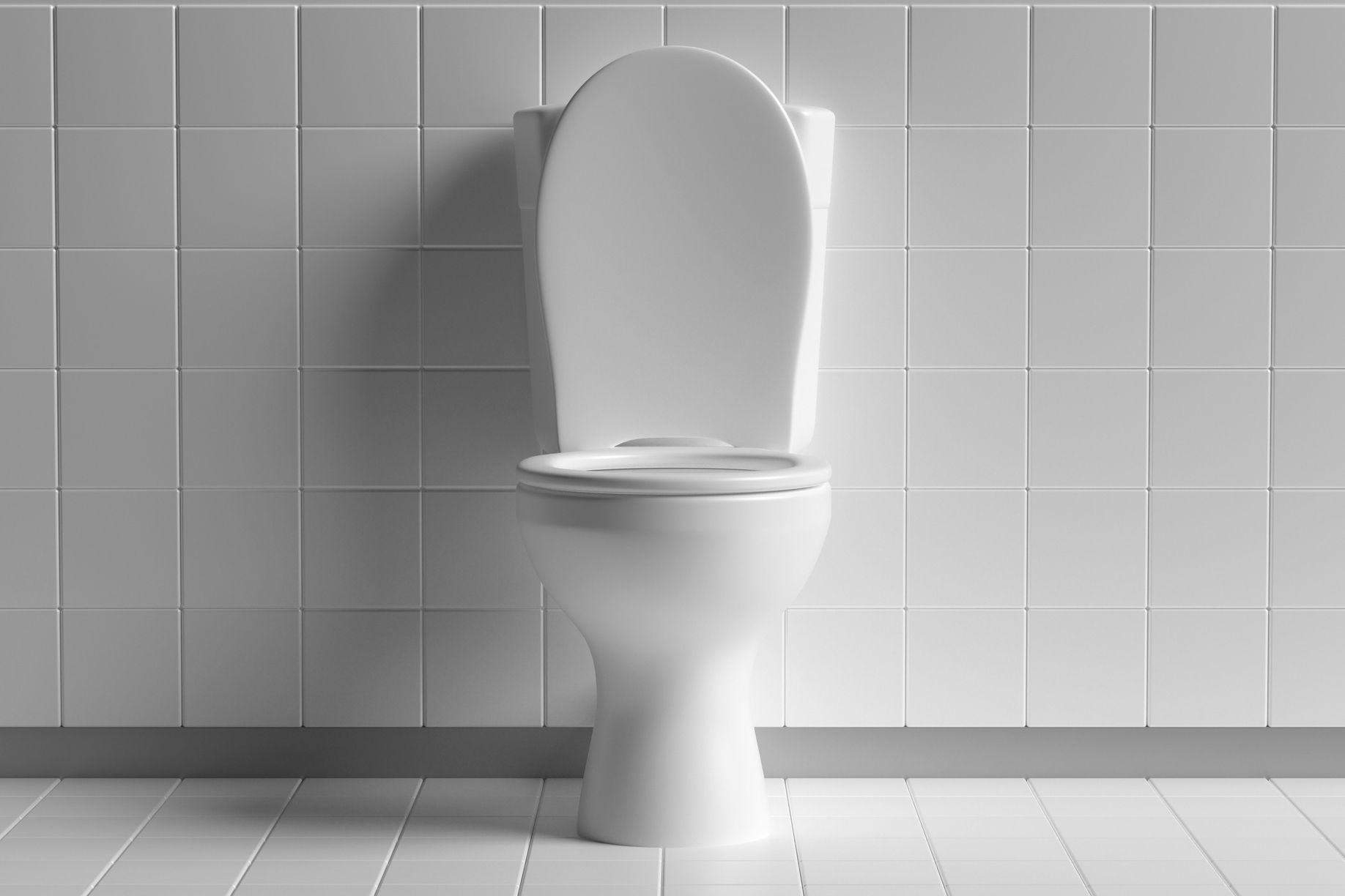 Clean white toilet bowl with white tiled floor and wall