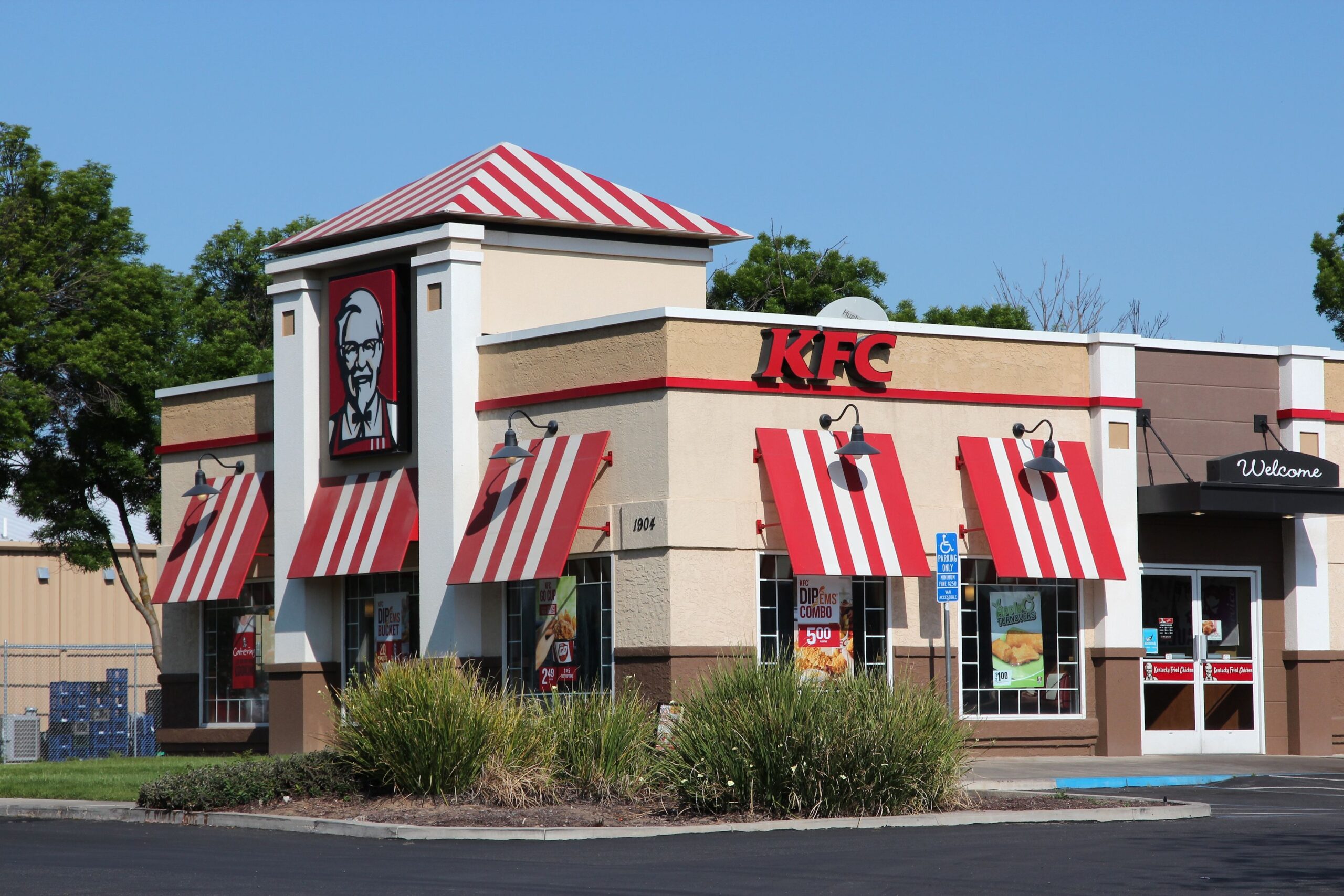 Exterior of a KFC fast food restaurant in Fresno, California with front doors and surrounded by parking spaces on a clear sunny day during summer