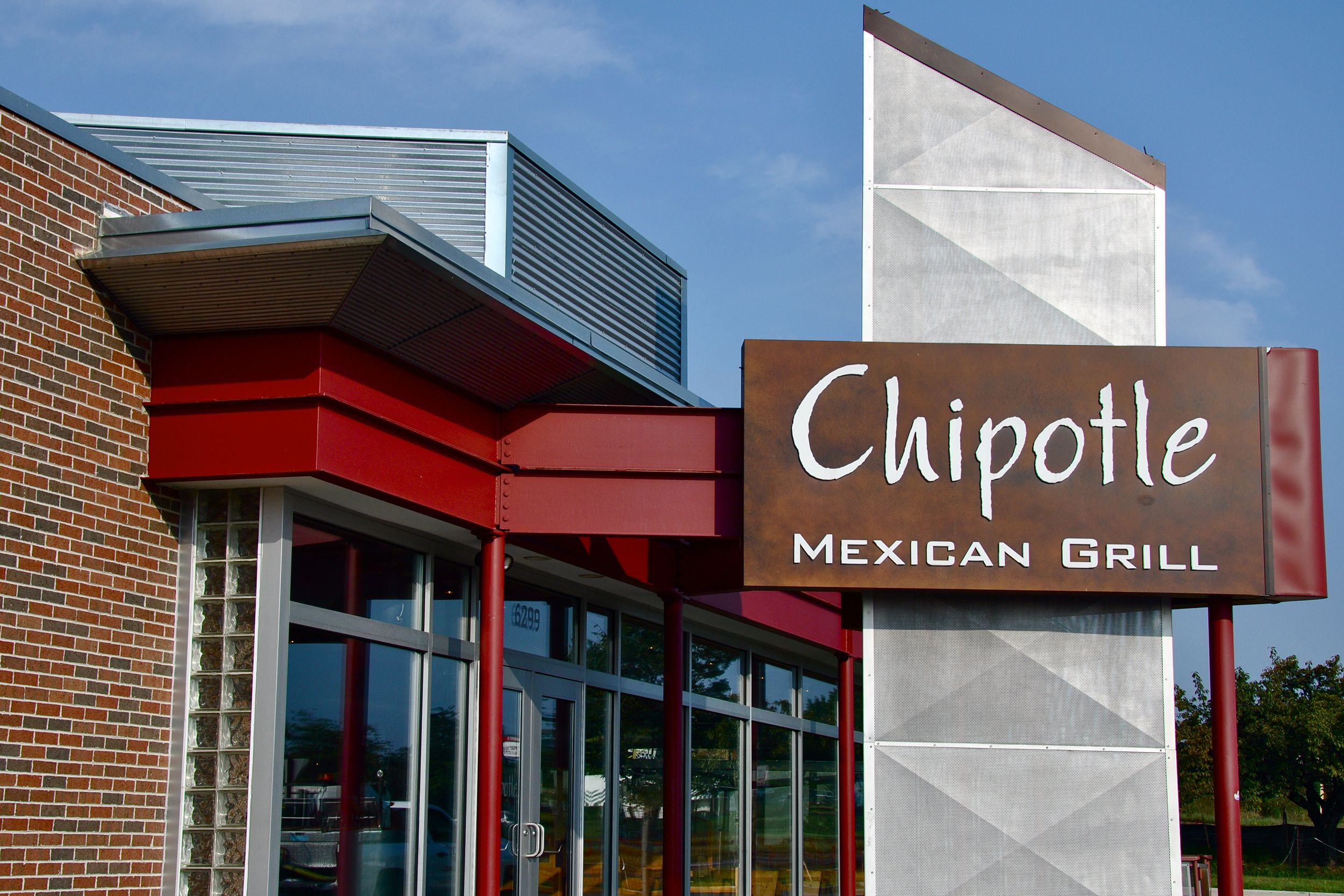 Focus on sign of Chipotle Mexican Grill in Falls Church, Virginia with exterior of restaurant in the background, against a blue sky on a sunny day