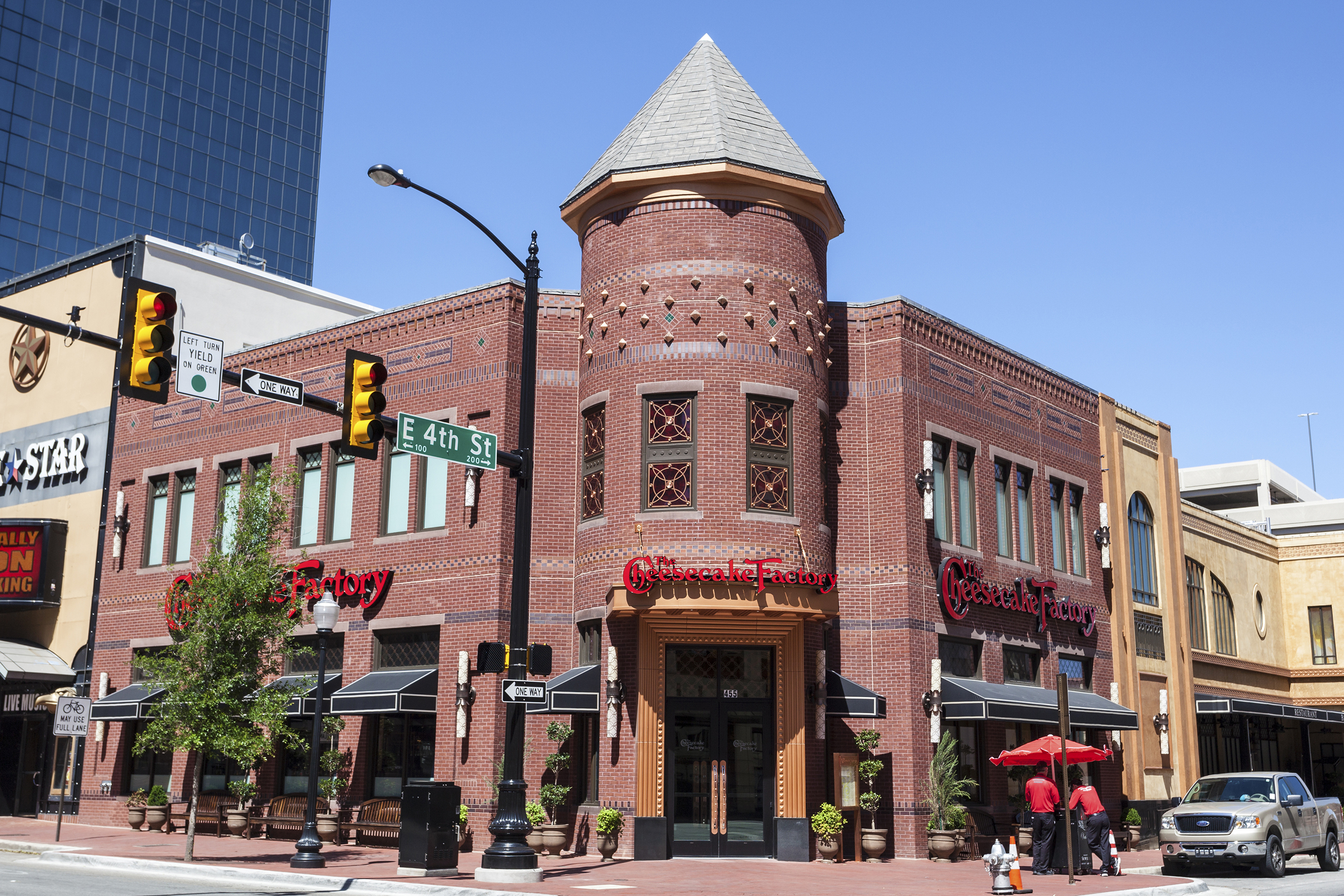 Focus on The Cheesecake Factory restaurant in downtown Fort Worth, Texas at the corner of an intersection, showing sidewalk, traffic lights, and road