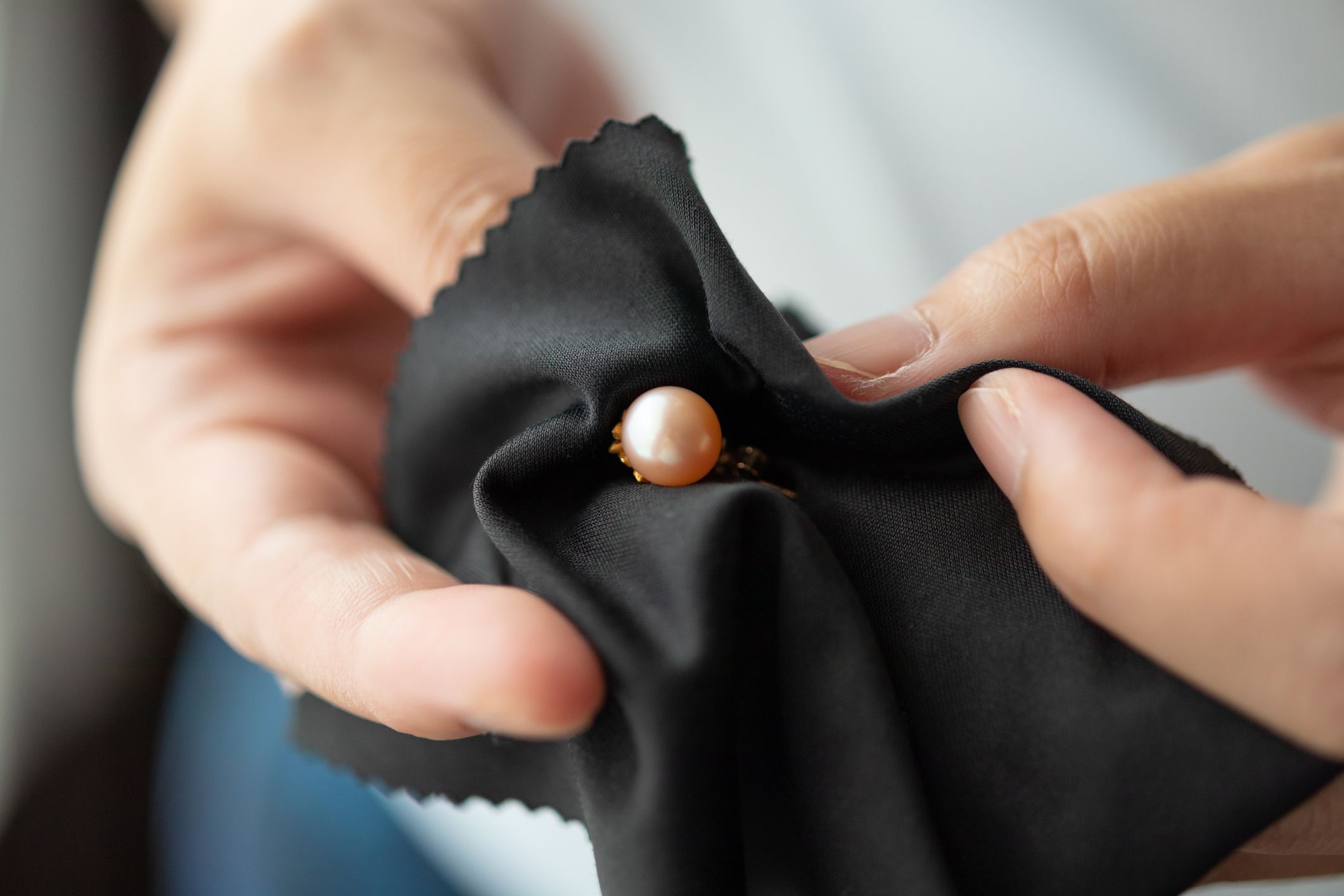 Two female hands cleaning a pearl earring with black fabric cloth