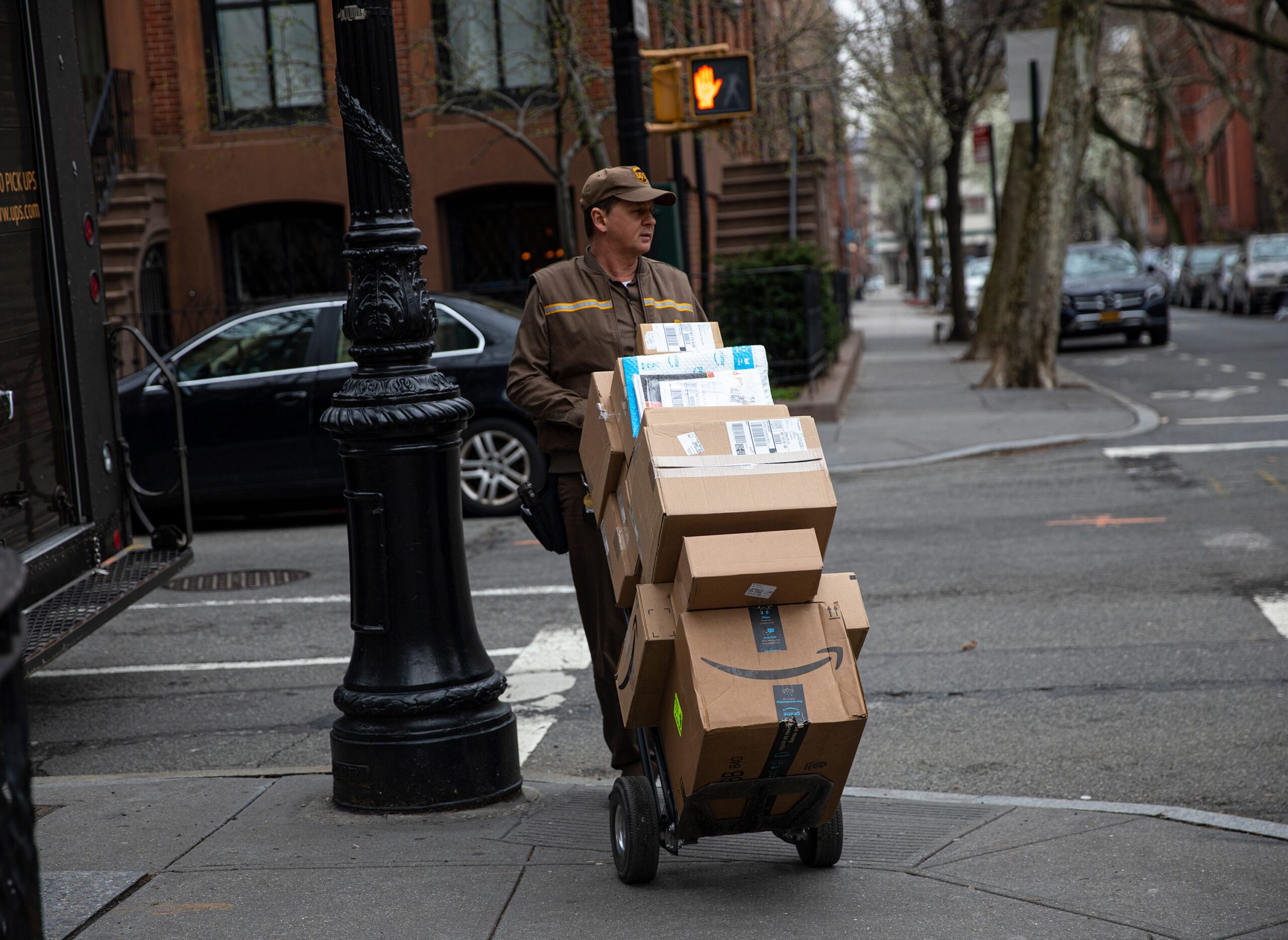 A delivery man for United Parcel Service, UPS, moves his hand truck loaded with packages through a residential neighborhood in Brooklyn, New York on March 30, 2020.