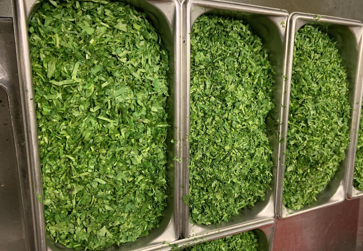 Three metal containers filled with finely chopped fresh green herbs, arranged side by side in a kitchen setting.
