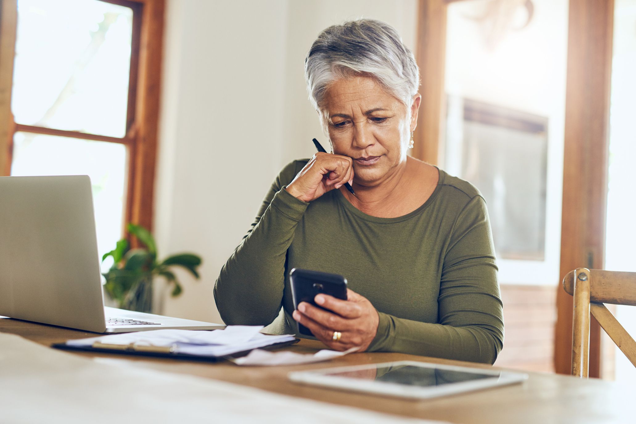 woman looking at phone, laptop and papers with worried expression