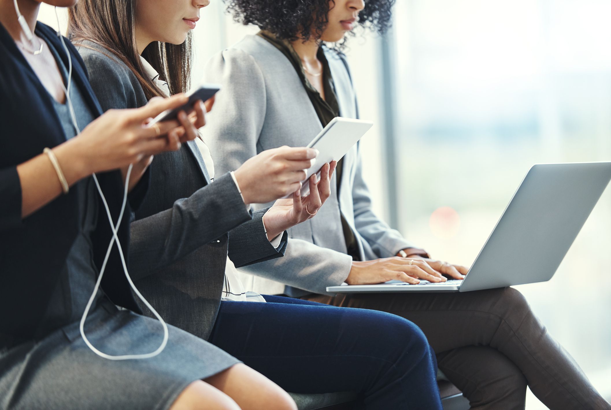 Shot of a group of young businesswomen using their wireless devices in a waiting room