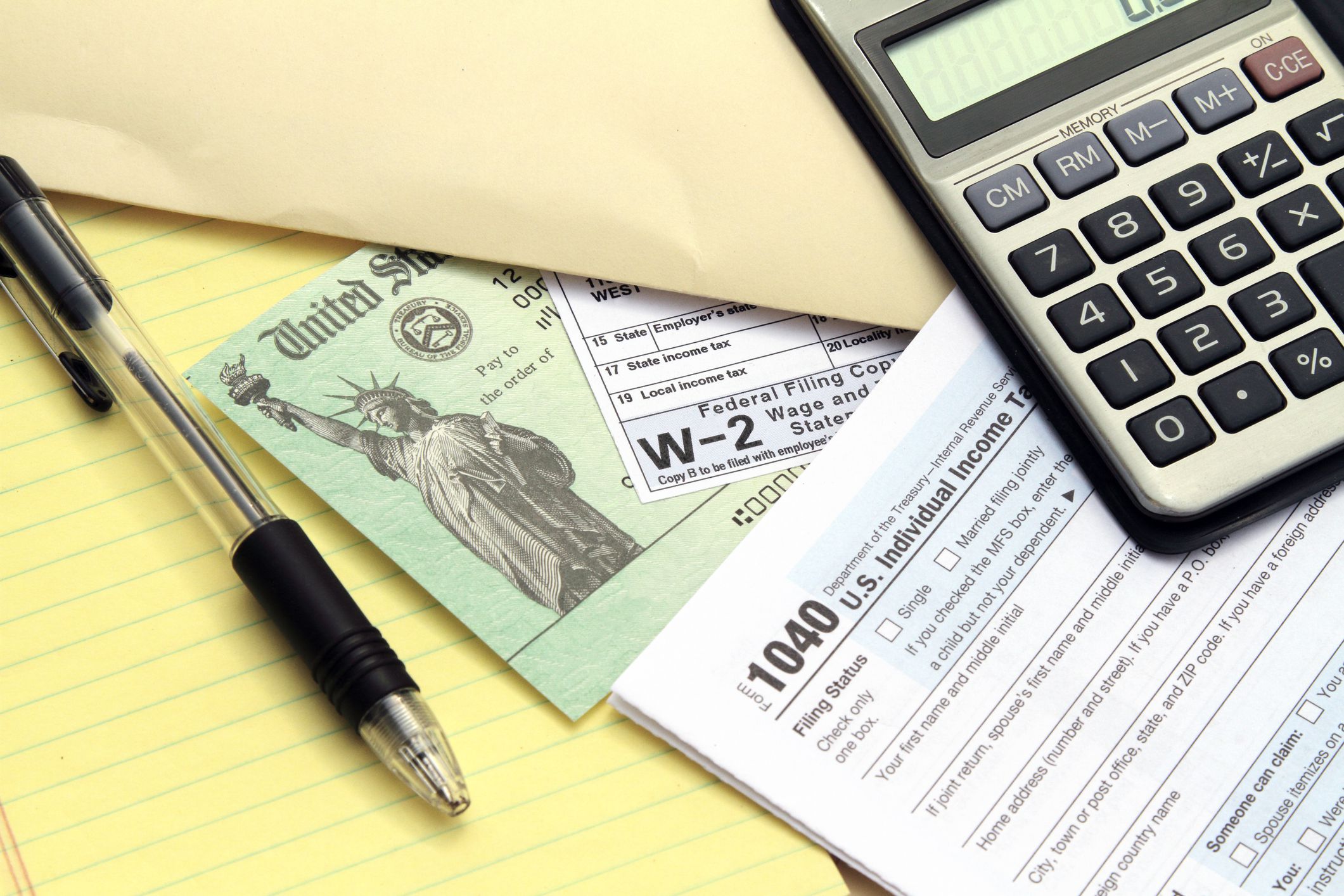 Tax forms with Treasury check. IRS tax forms 1040 and W-2. Tax preparation concept. Treasury check represents a tax refund. Calculator, pen and papers yellow note pad also visible.