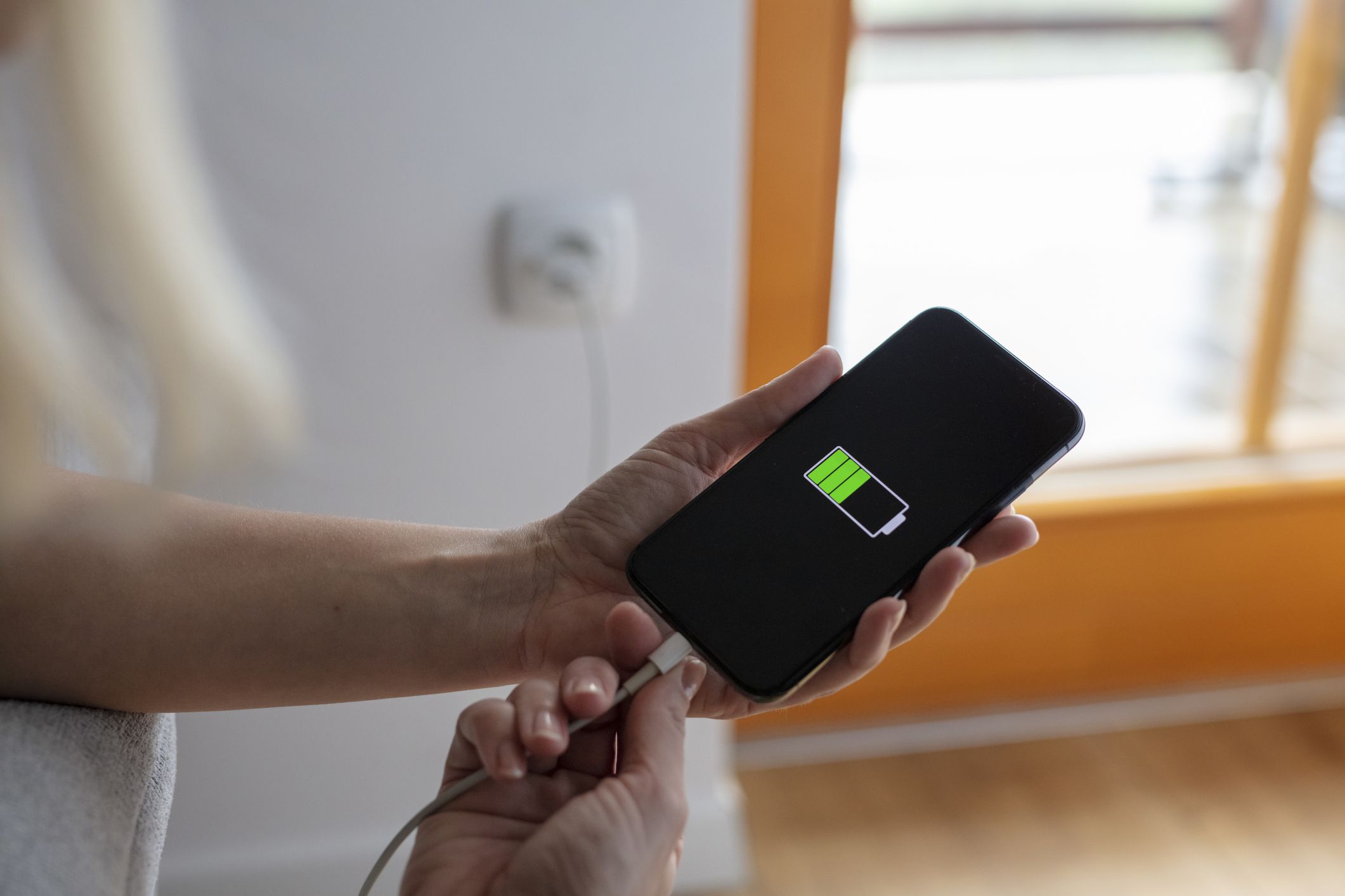 Hands plugging in and charging smart phone with USB cable at wall