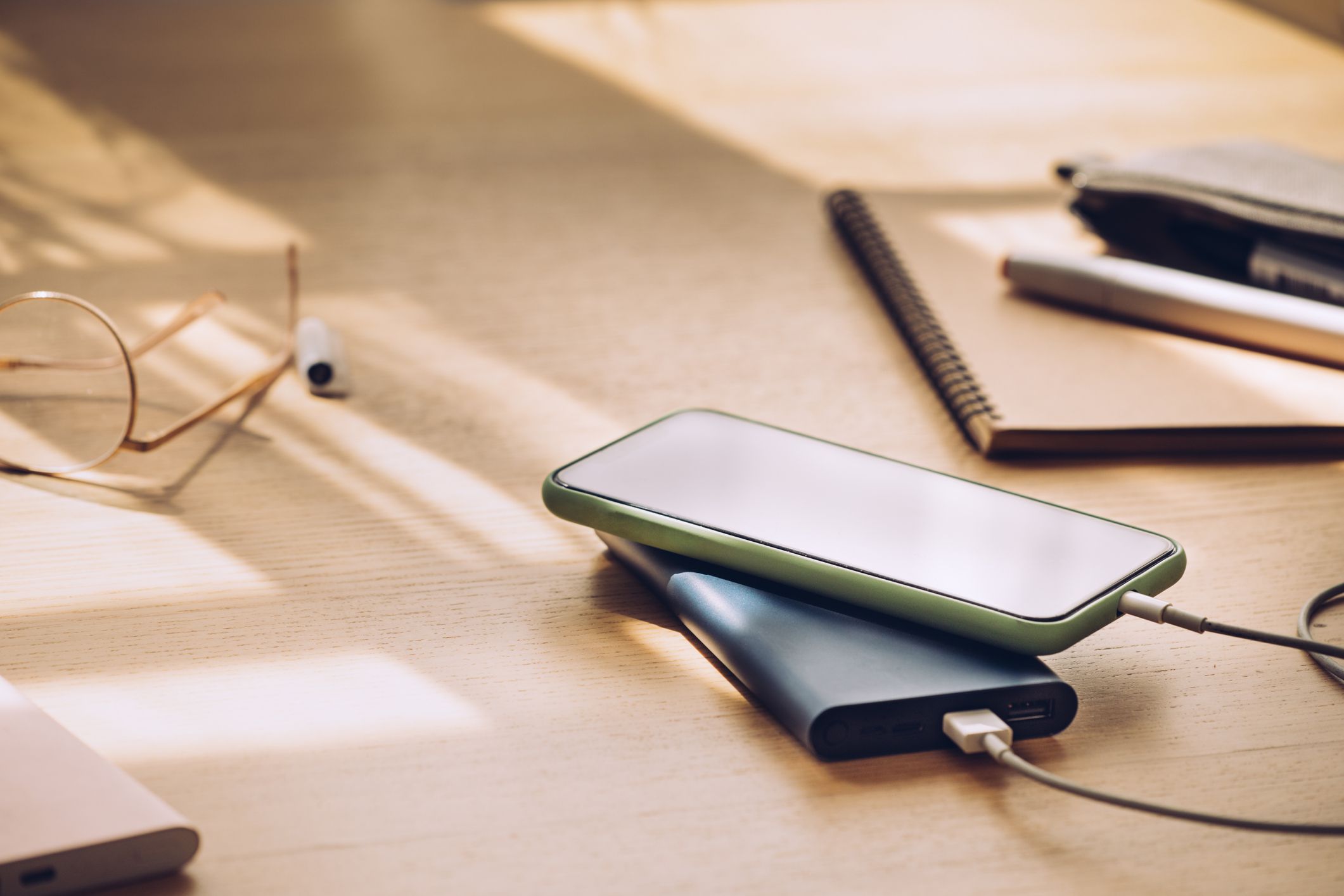 Smartphone charging through a portable battery laid on a wooden desk.