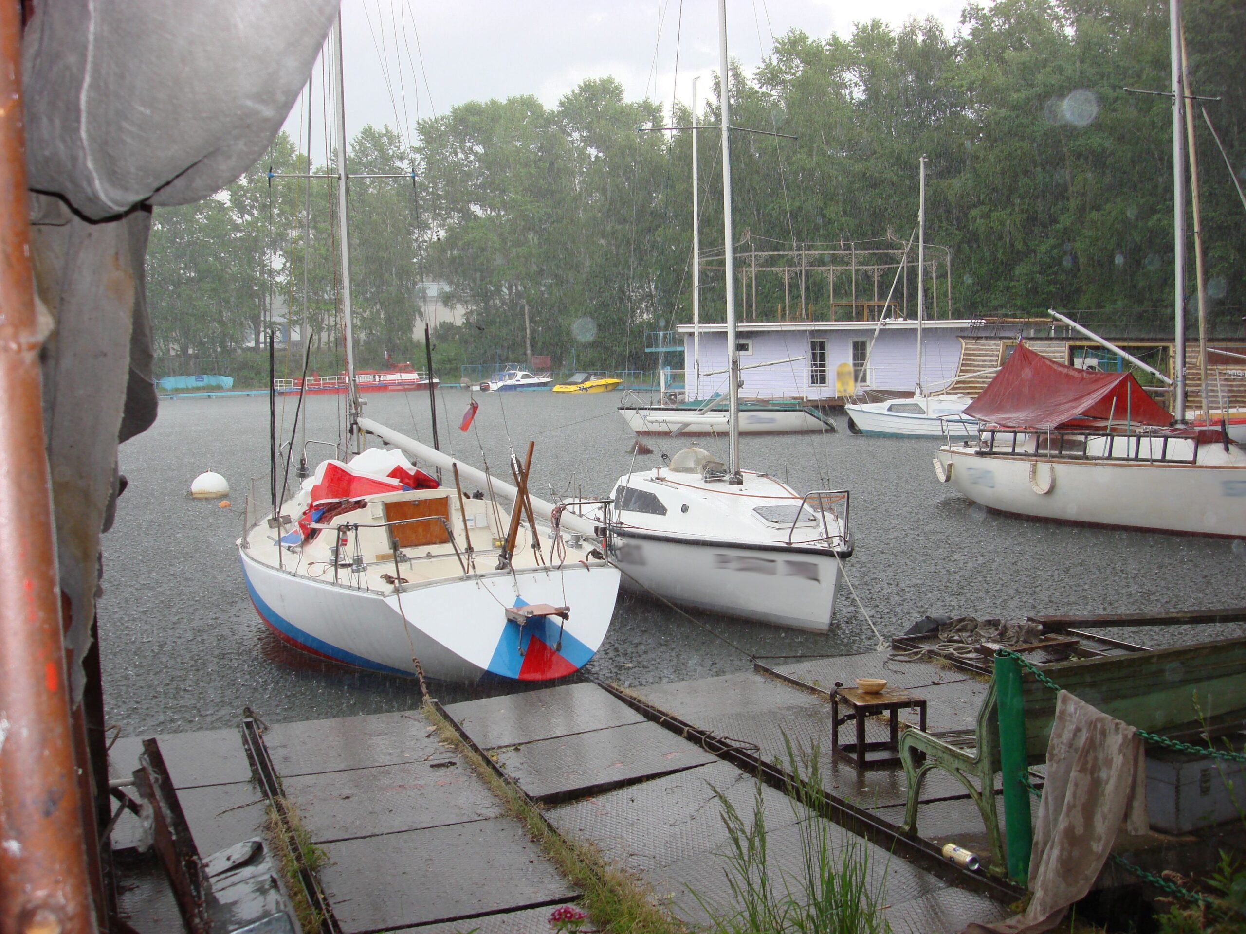 Yachts in the rain in the marina, in the yacht club. The summer rain comes straight. Huge drops break on the surface of the lake