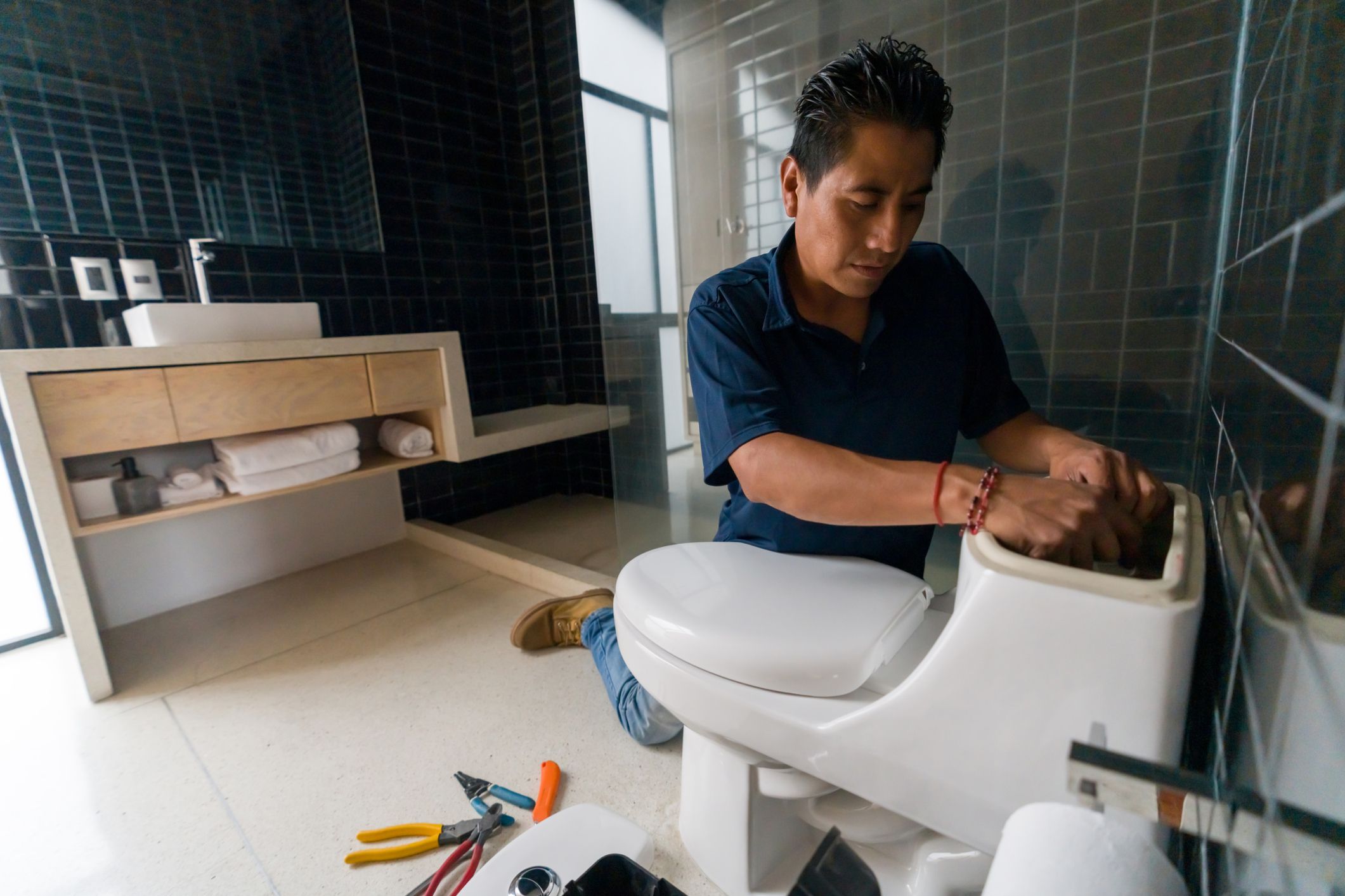 Latin American plumber fixing a toilet in the bathroom - home repair concepts