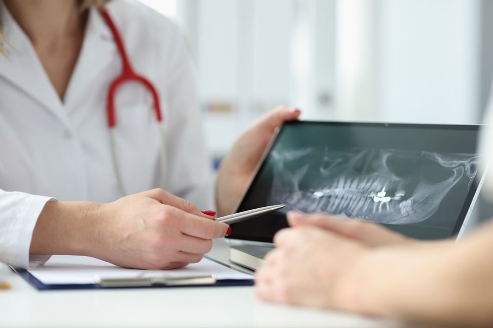 Dentist showing patient tablet with x-ray of teeth in clinic closeup