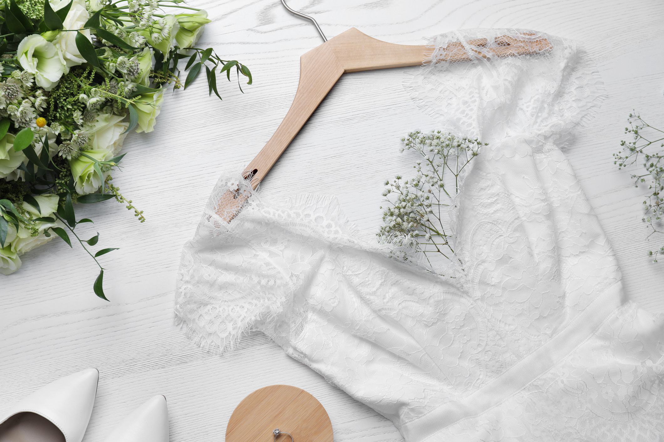 Beautiful wedding dress, engagement ring and flowers on white wooden background, flat lay