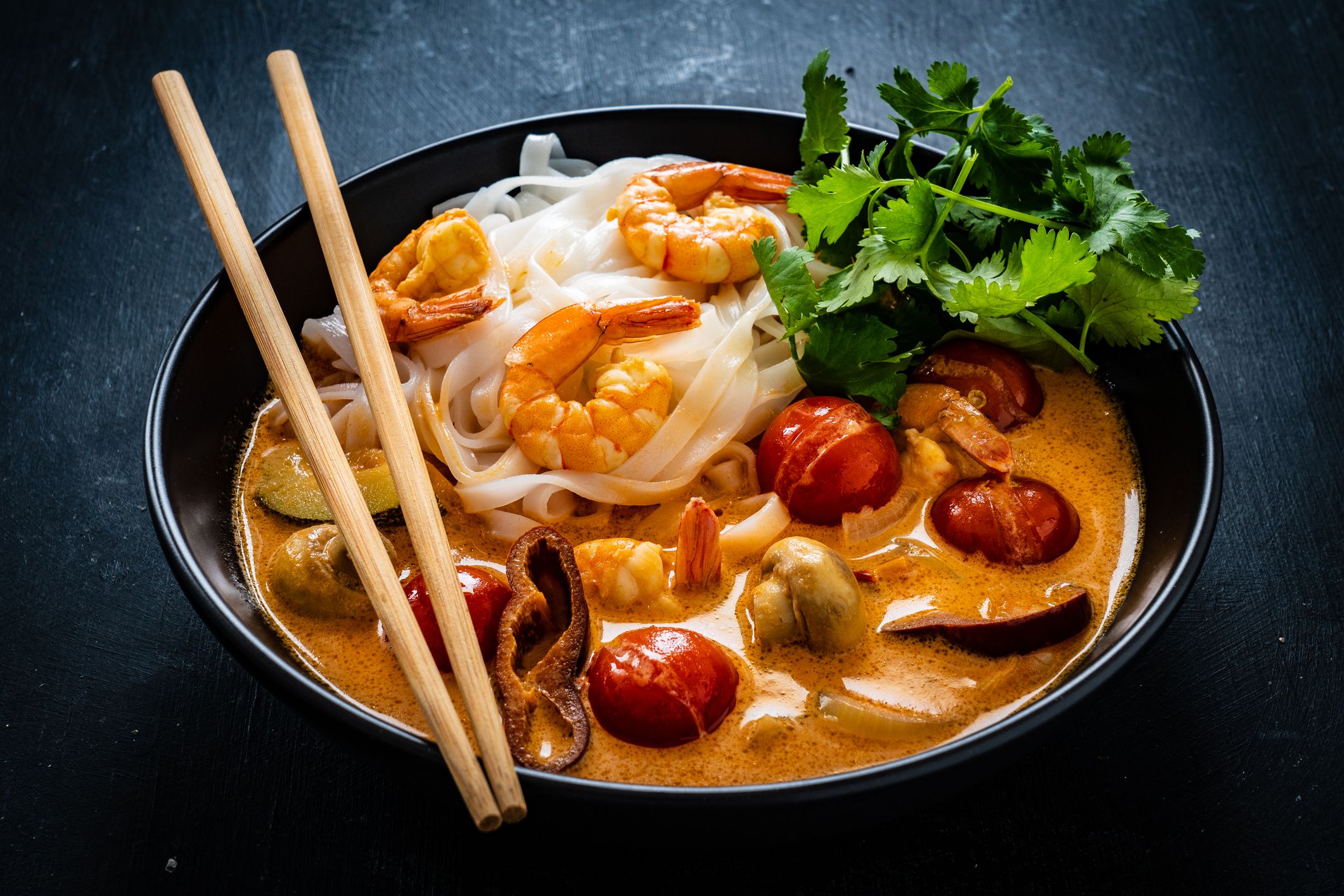 Tom Yum - Thai soup with prawns and rice noodles on black wooden table