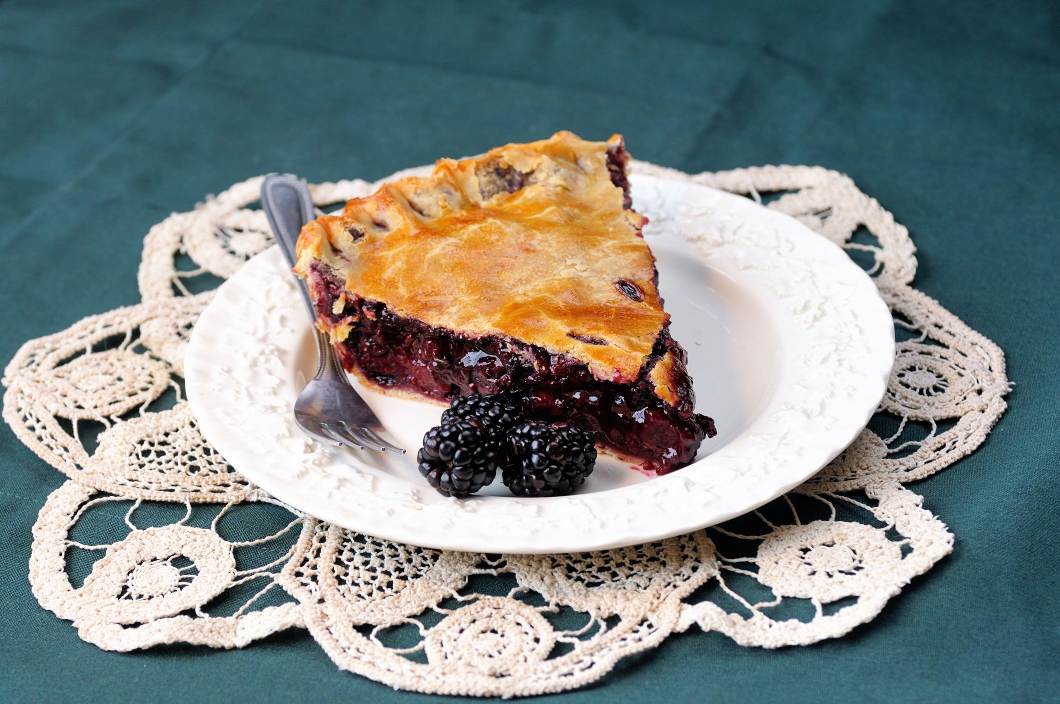 Freshly baked blackberry pie slice sitting on a pretty plate and doily.