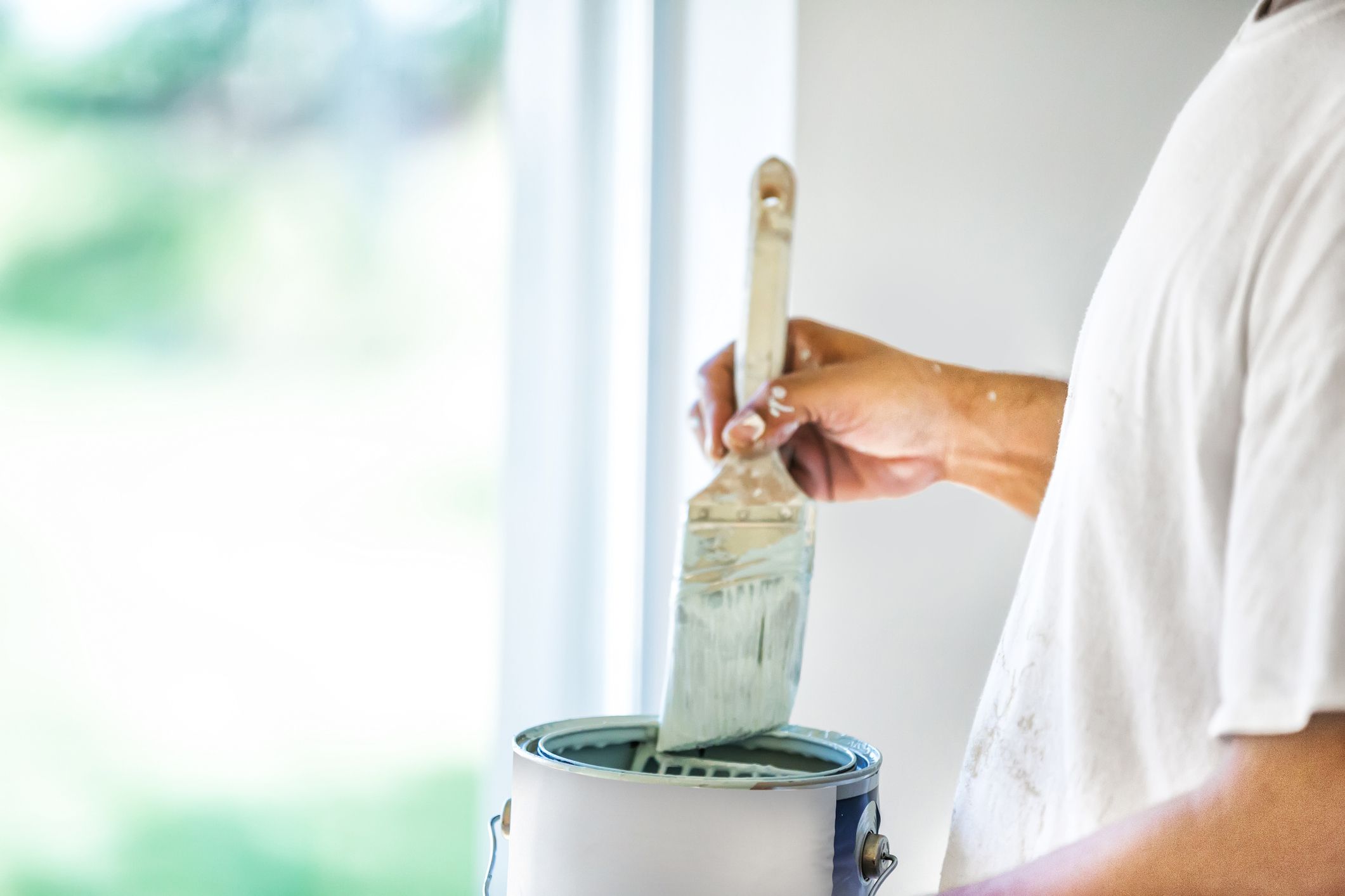 A house painter dips his brush into a can of paint. rr