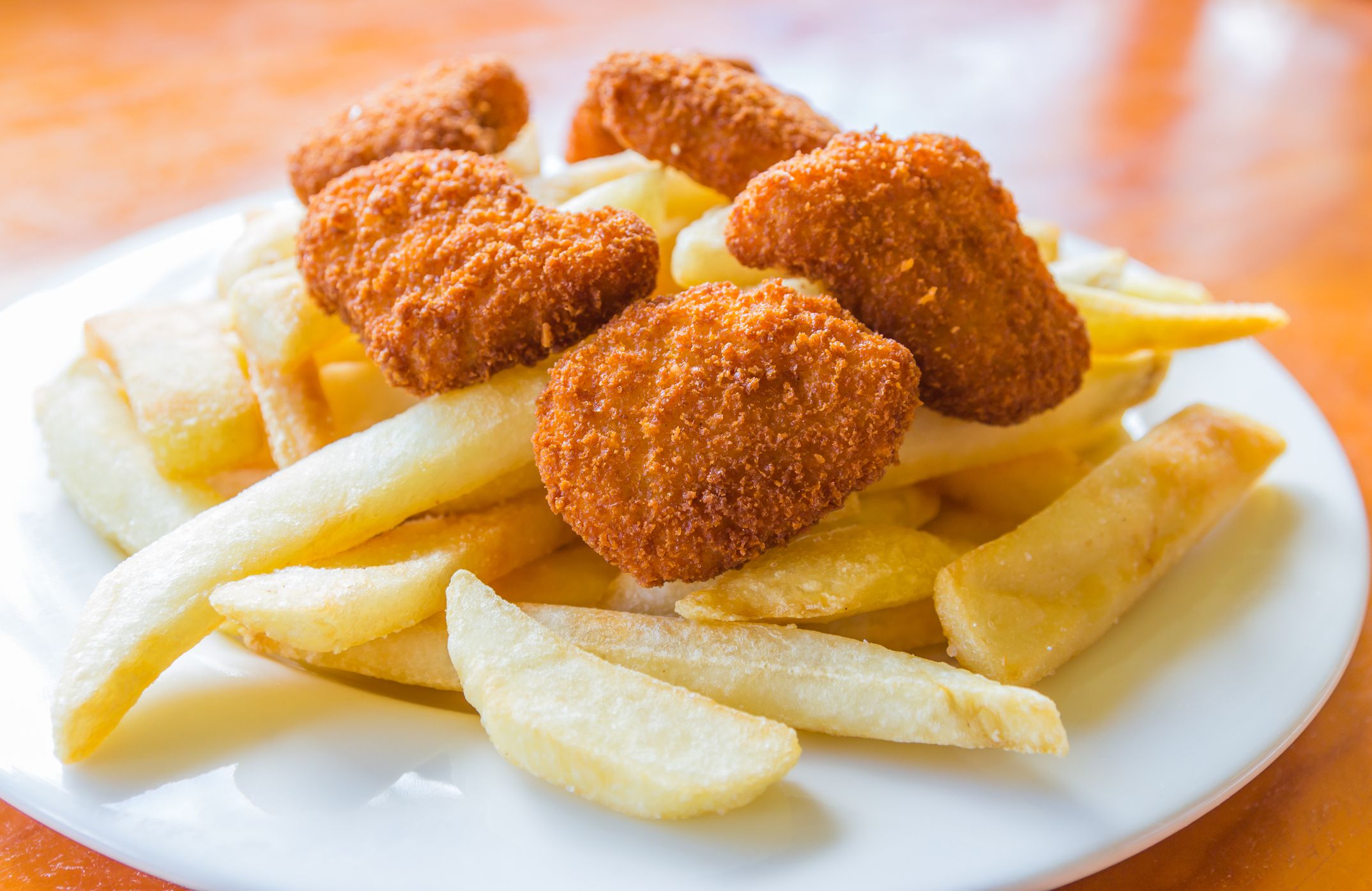 The deep fried potato chips and chicken nuggets on the white dish with the wooden table