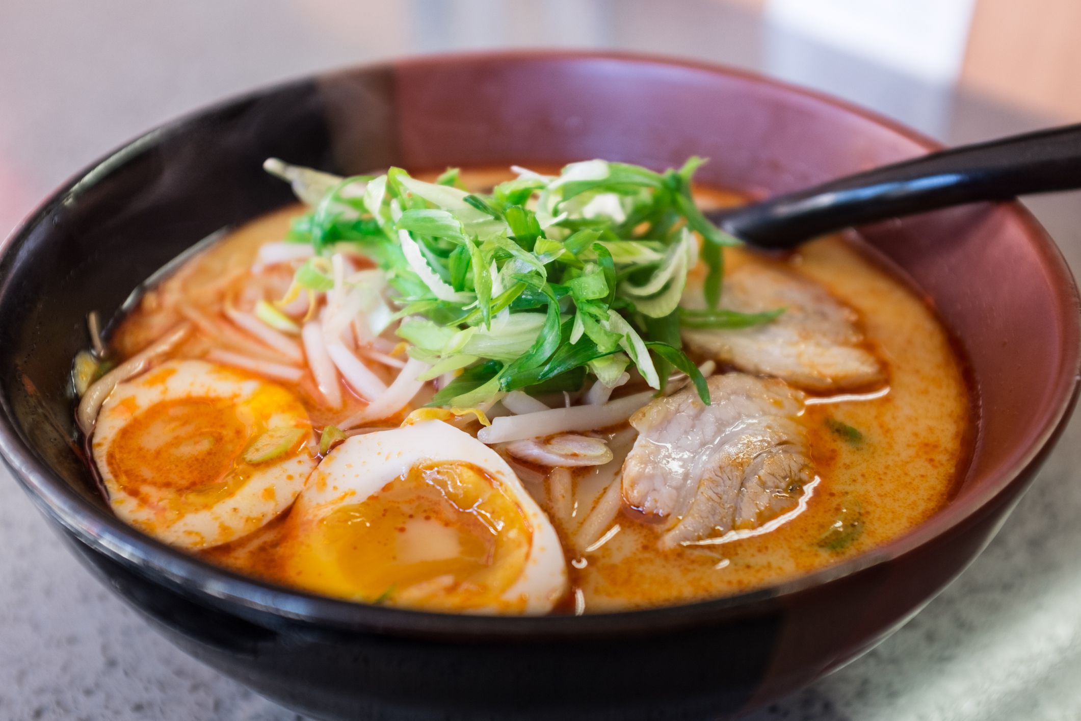 Daylight macro photo of Japanese ramen noodle soup with pork, scallions, sprouts, bone broth, and hard-boiled egg.