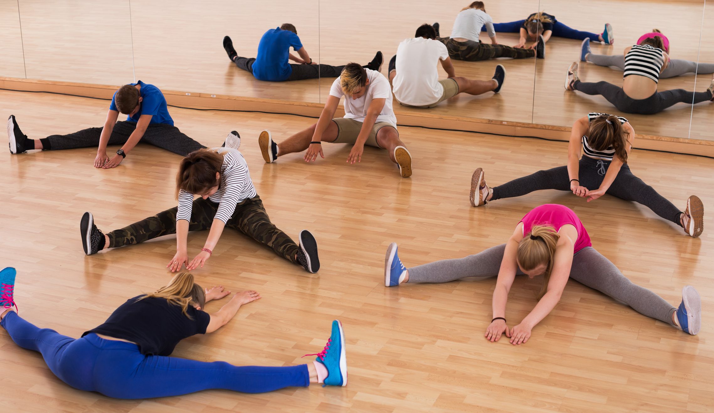 Group of teenage students with female instructor stretching in dance hall