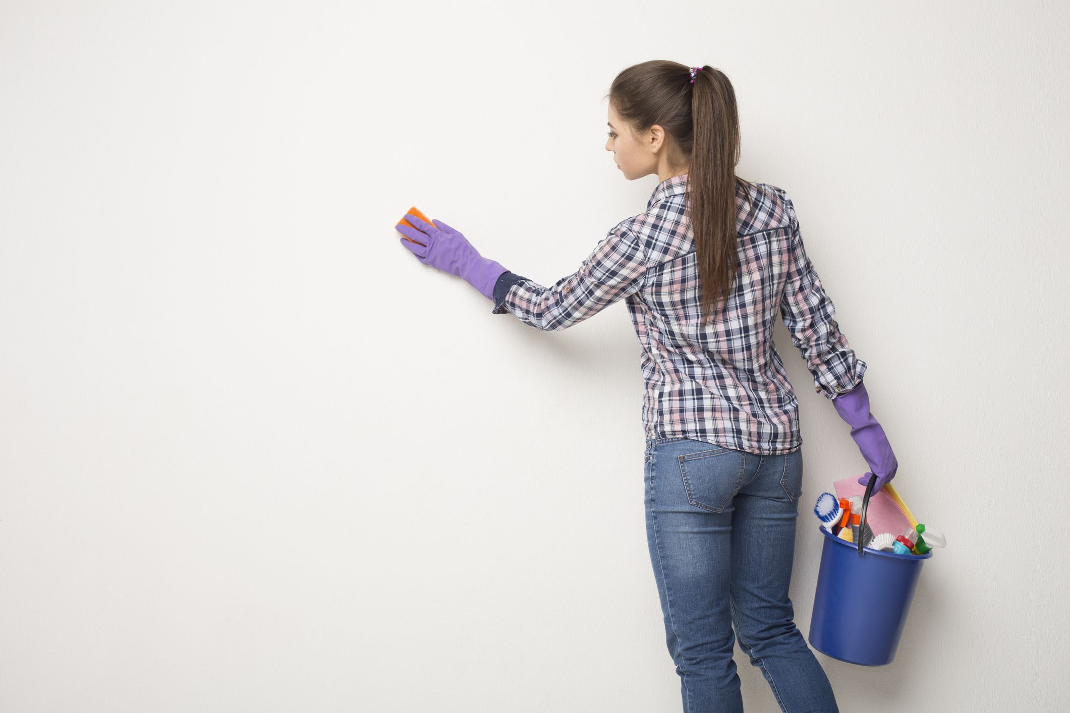 Woman wiping white wall from dust with dry rag, back view. CLeaning service or regular clean up concept, copy space