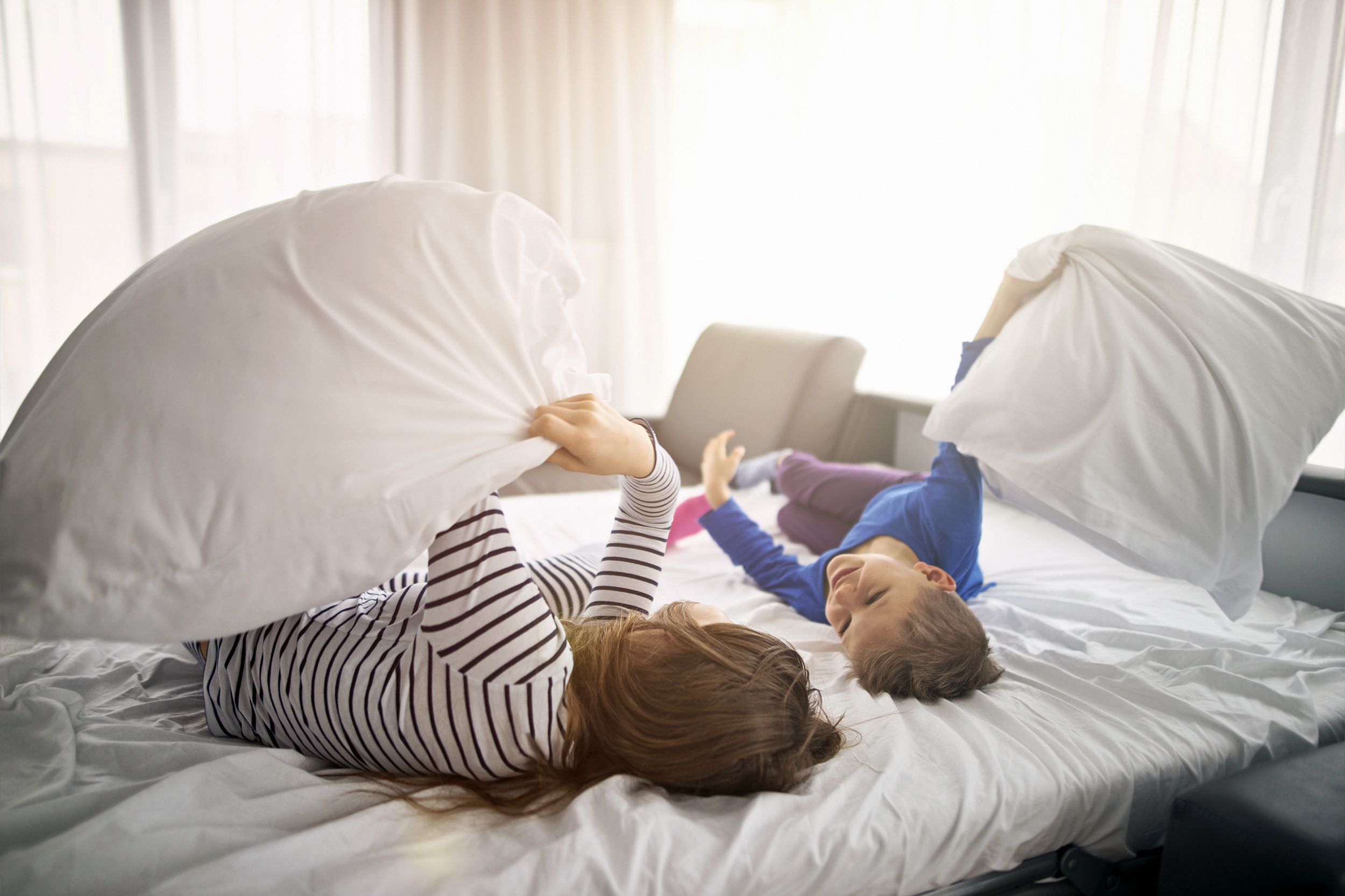 brother and sister having a pillow fight on sunny morning