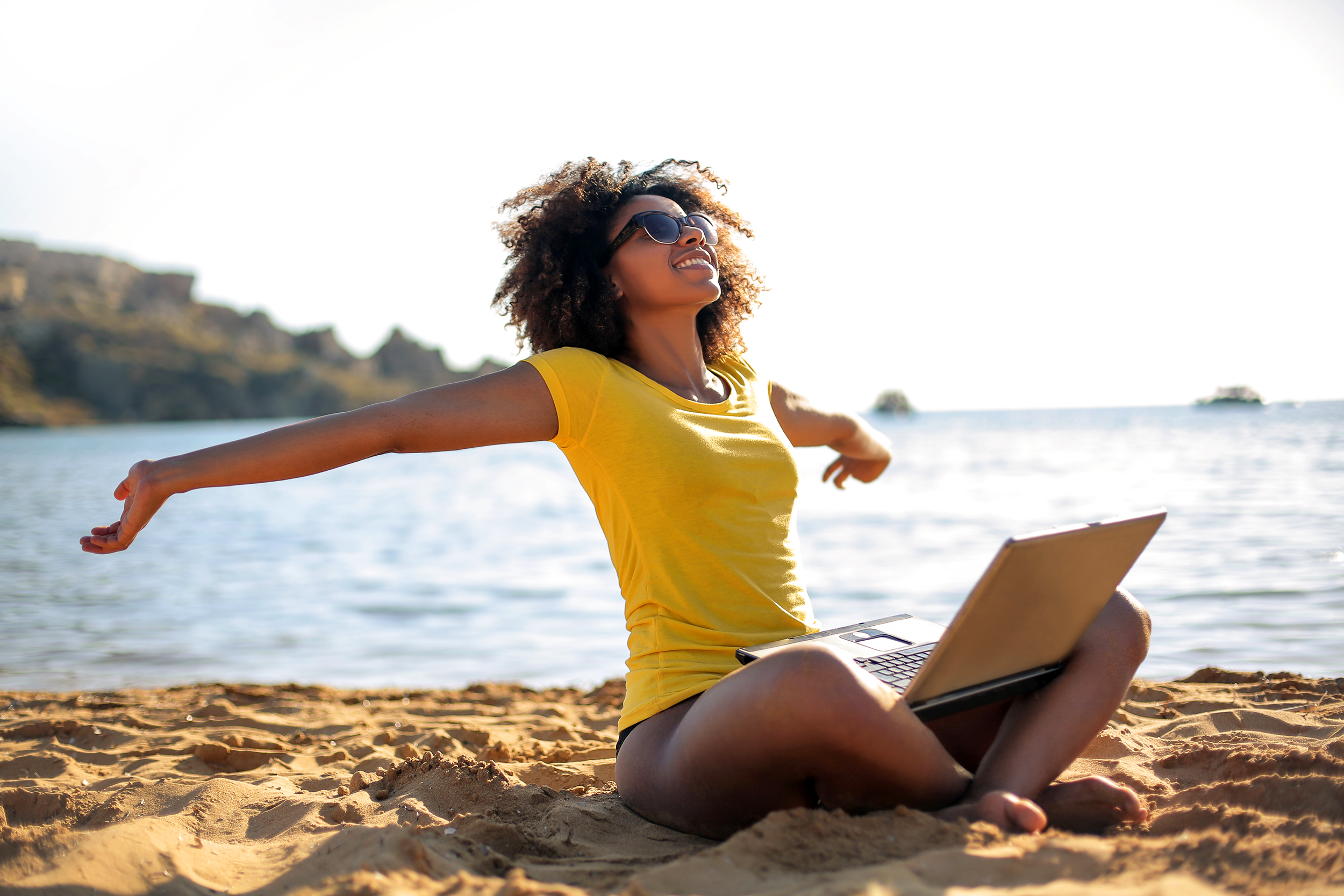 Happy woman sitting on the beach with her laptop