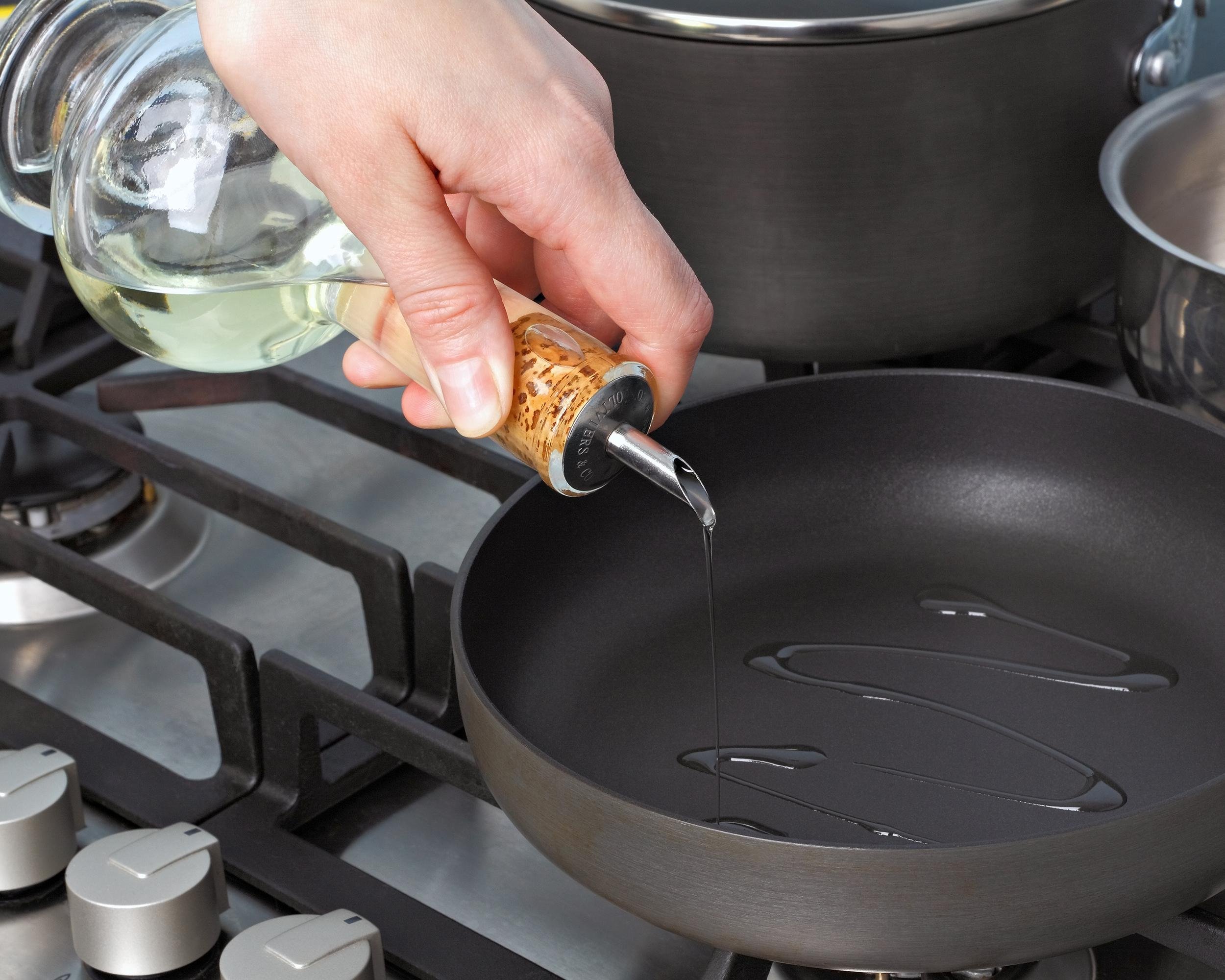 hand pouring oil on pan on stove