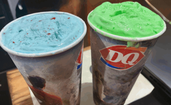 Two Dairy Queen cups filled with thick ice cream; one is light blue with red specks, and the other bright green—these unique treats could be Dairy Queen Blizzards or even creations from the Dairy Queen secret menu, both sitting on a table.