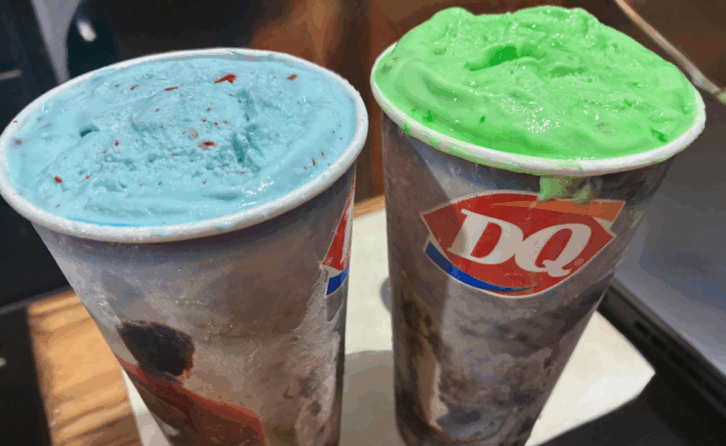 Two Dairy Queen cups filled with thick ice cream; one is light blue with red specks, and the other bright green—these unique treats could be Dairy Queen Blizzards or even creations from the Dairy Queen secret menu, both sitting on a table.