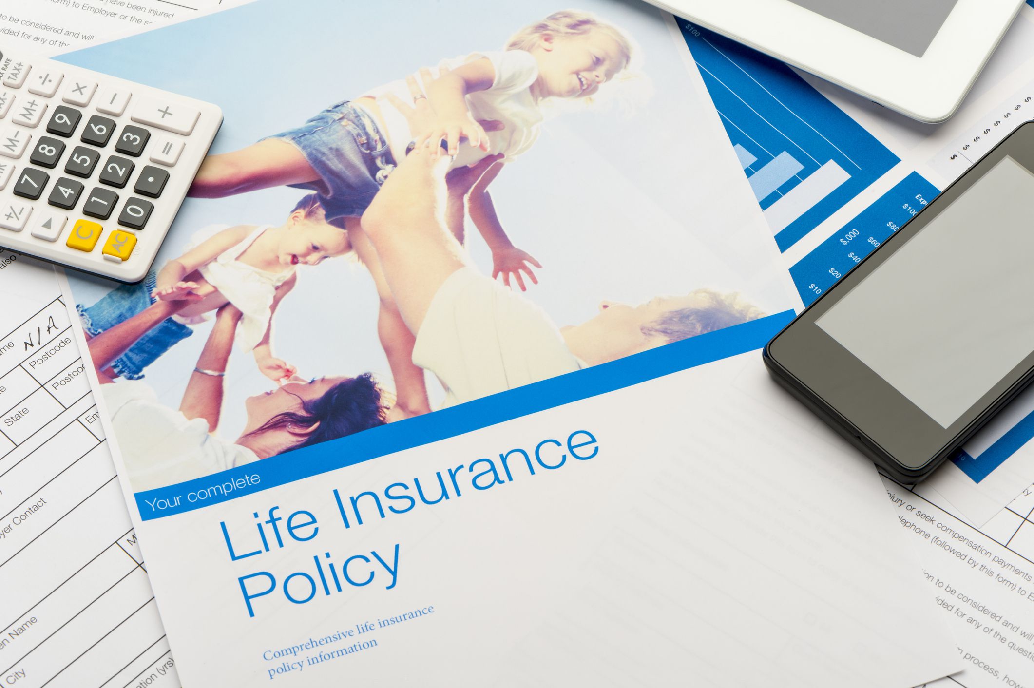 Life insurance policy documents and forms with a calculator, a smartphone, and a tablet, top document has image of a happy family