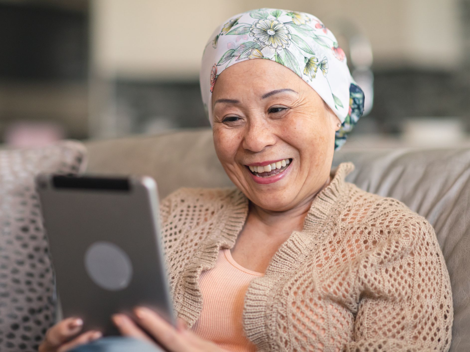 The happy woman is using a digital tablet to video message friends and family. She is spending time at home. The woman is smiling at the screen.