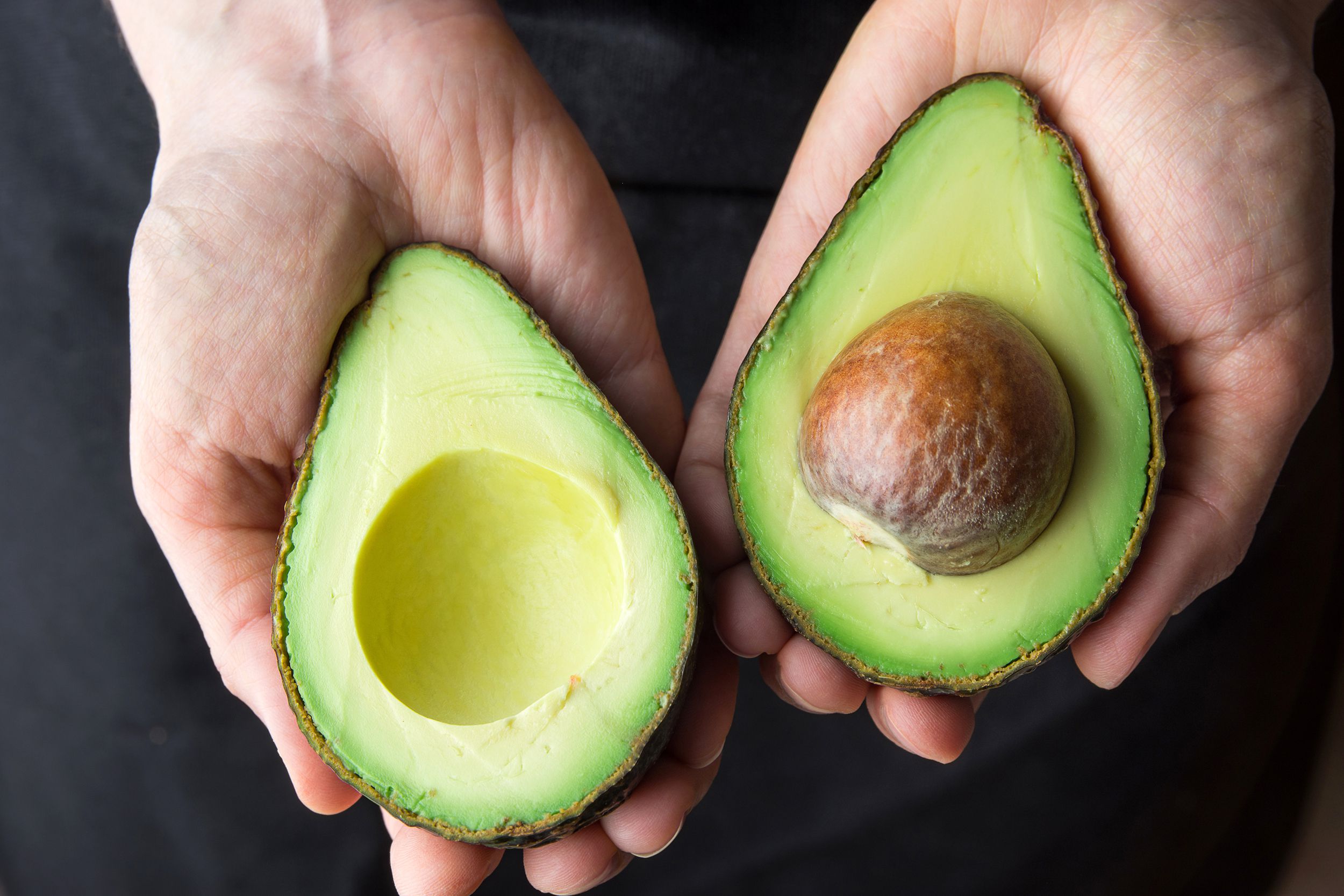 Hand holding opened avocado with pit