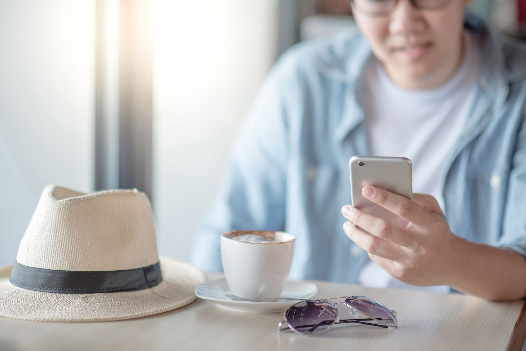 Asian man using smartphone while drinking coffee in the cafe. Relaxing time with entertainment and social media mobile app. Modern device for global communication. Internet of things concept