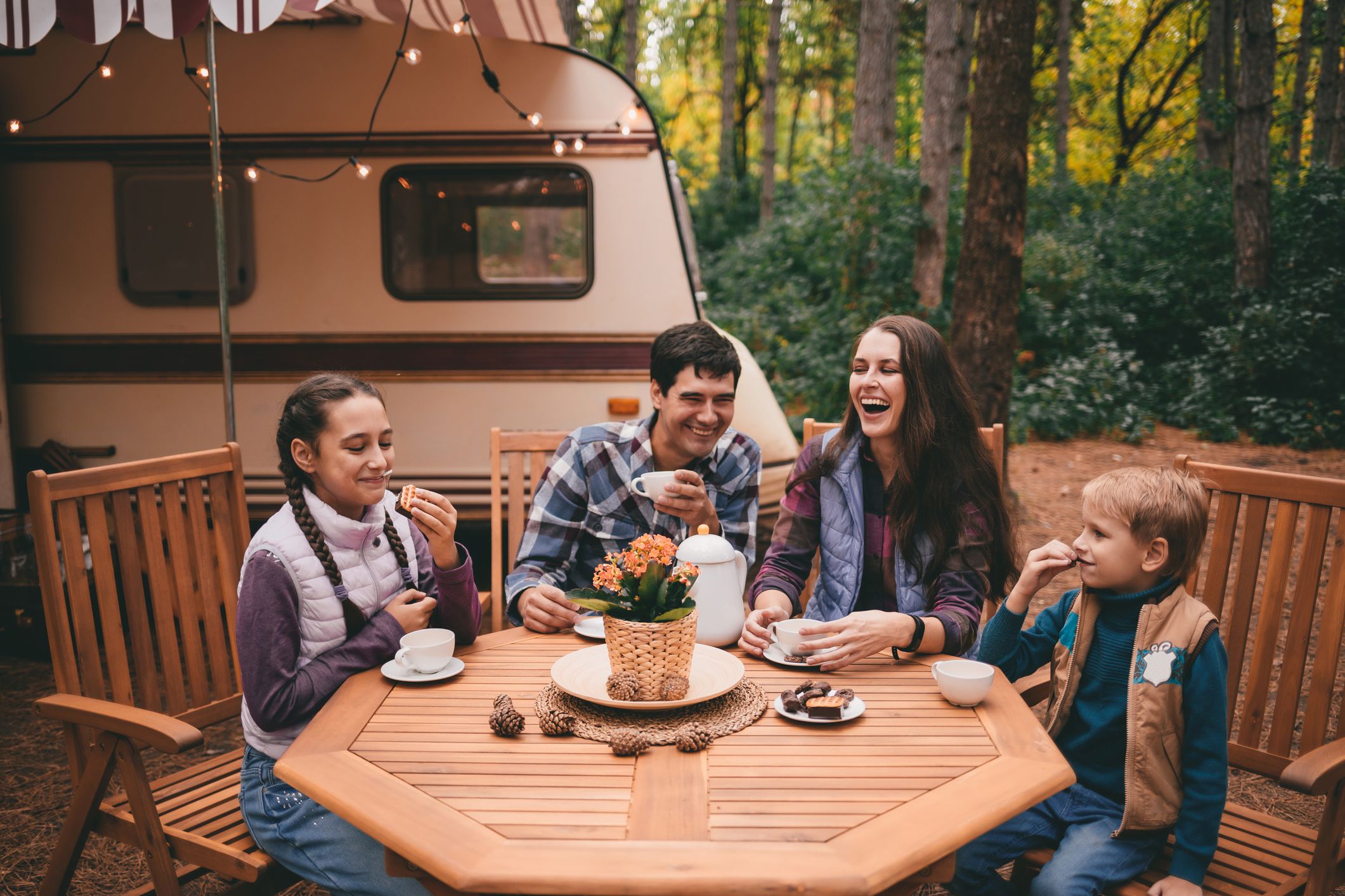 Happy family on a camping trip relaxing in the autumn forest. Camper trailer. Fall season outdoors trip.