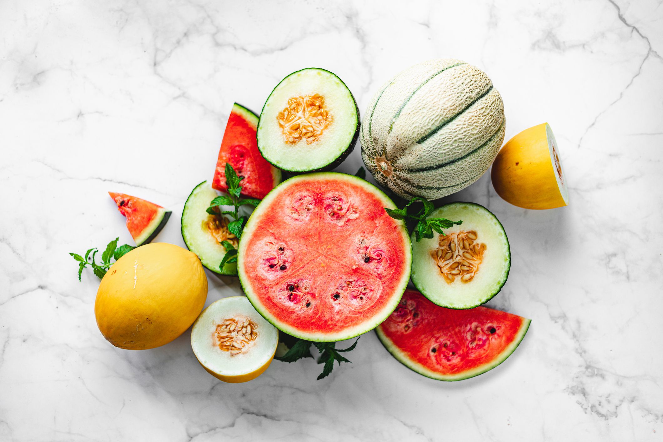 Directly above shot of exotic tropical fruits on white background. Various types of melons slices pver marble surface.