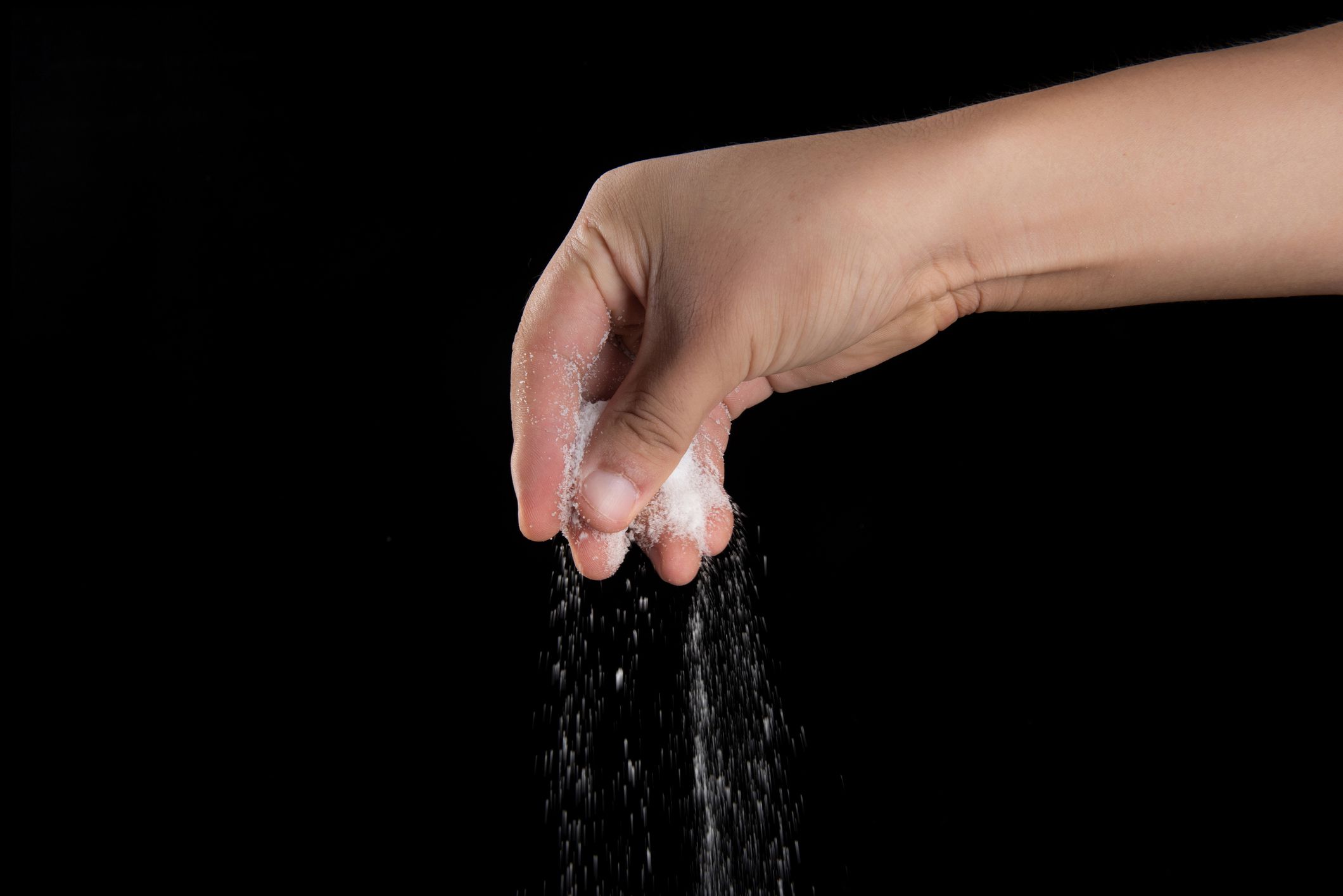 Male hand sprinkles salt on a black background. Cooking concept.