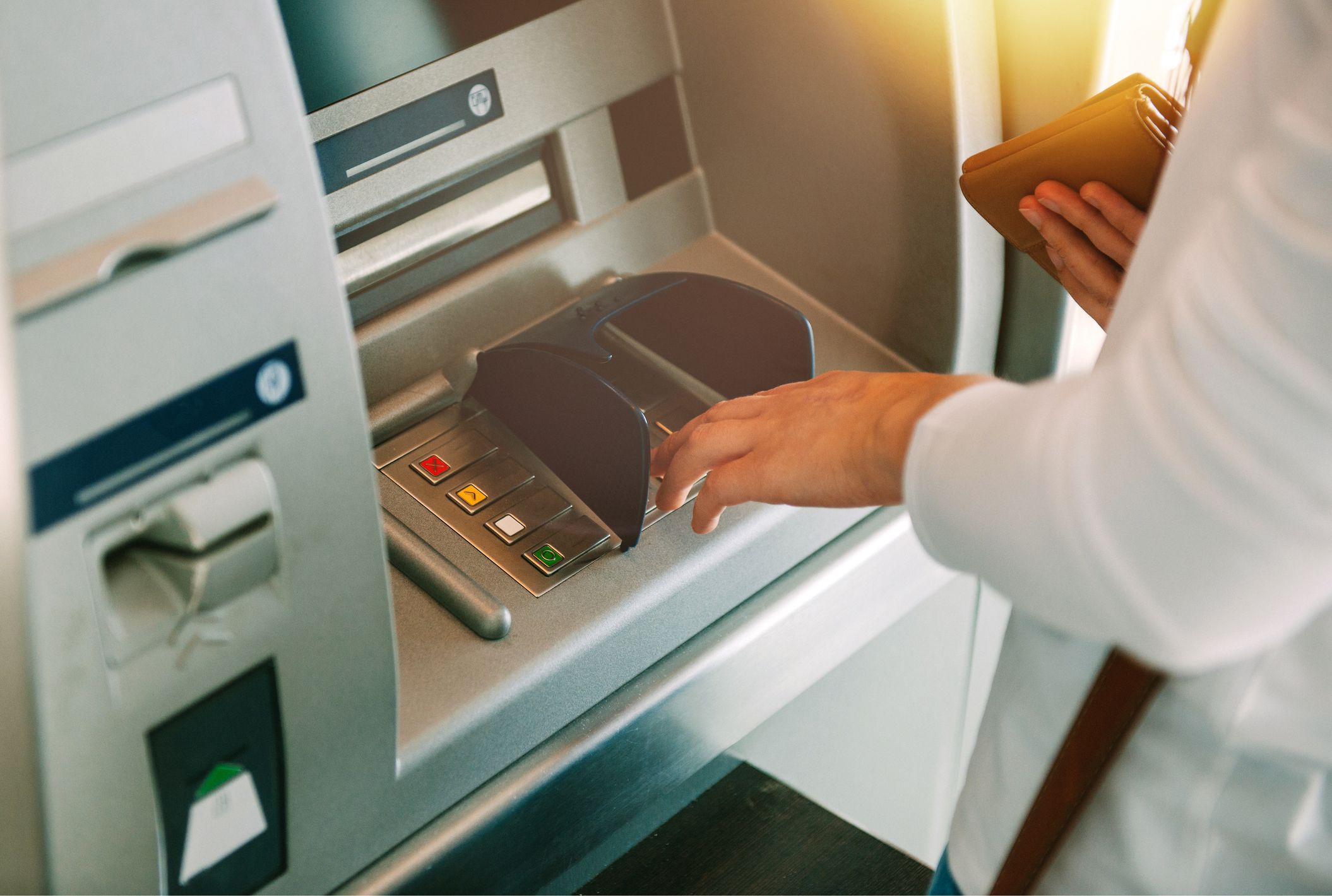 Woman using ATM holding wallet an pressing the PIN security number on the keyboard automatic teller machine