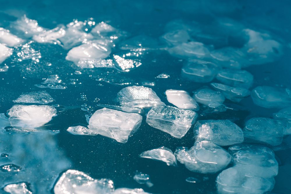 Cold water and ice cubes melting under the sun, background