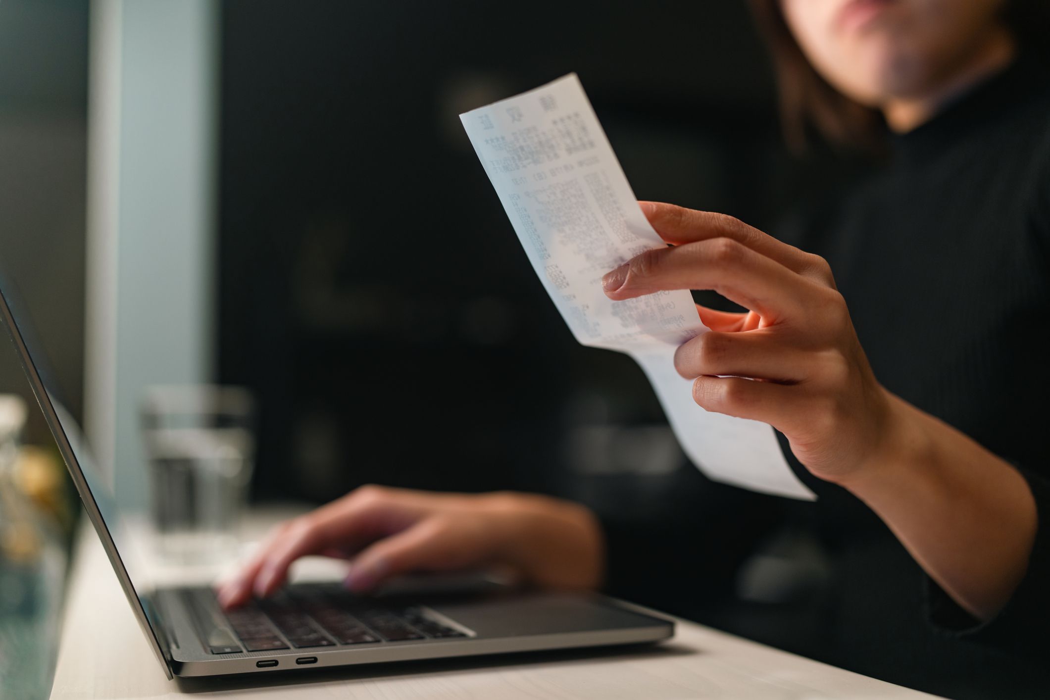 A close-up photo of a woman`s hands doing financial planning and checking receipts at home.