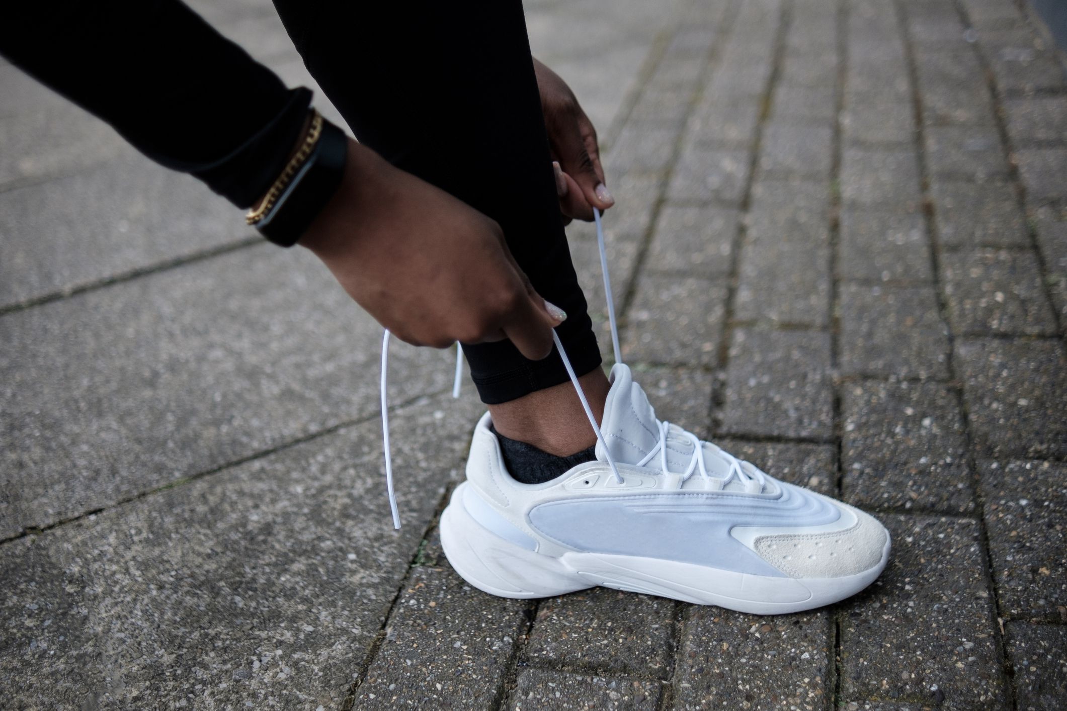Female hands tying sport shoes on the pavement. Shoes are white and she is wearing black leggings and sport watch.