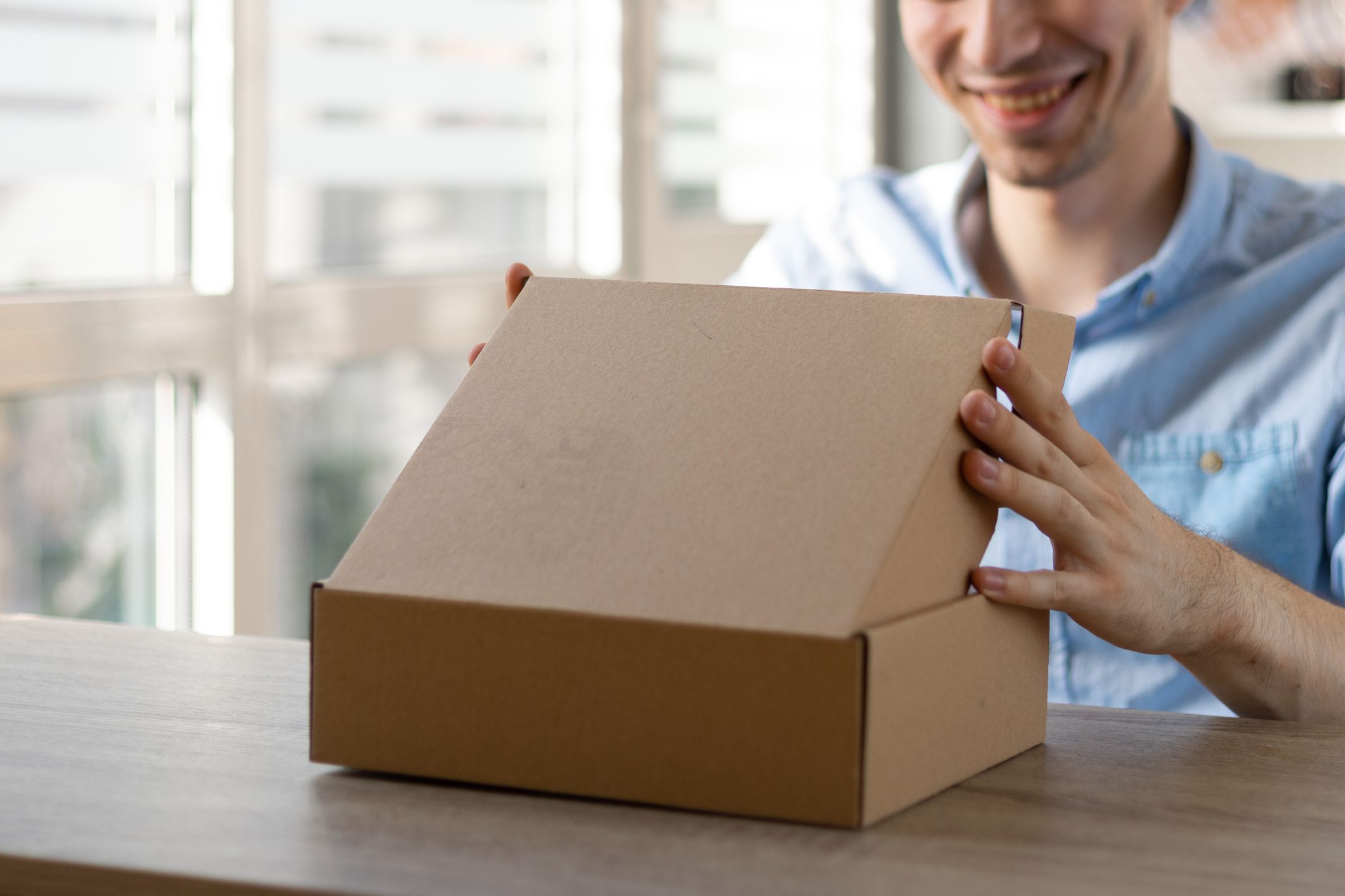 Smiling young guy has pleasure to receive package with consumer goods purchased online
