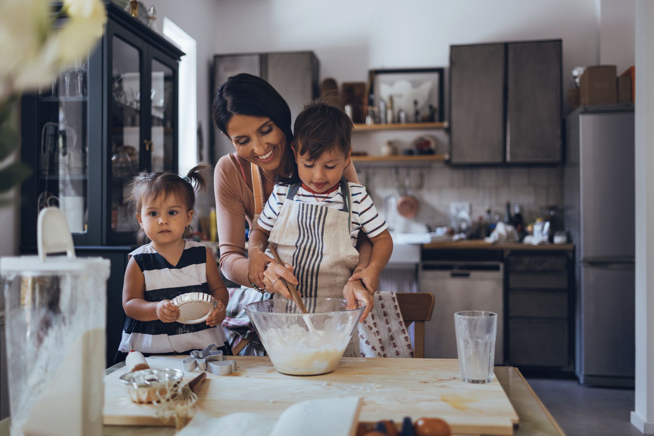 Caucasian mother and her two little children making a cake from the ingredients.