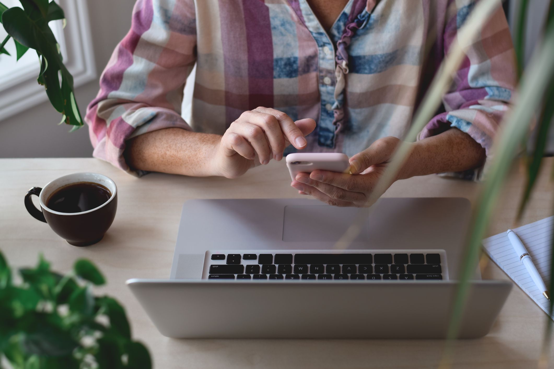 Hands of woman sitting at desk in front of laptop computer using mobile phone, using multiple devices concept, multitasking