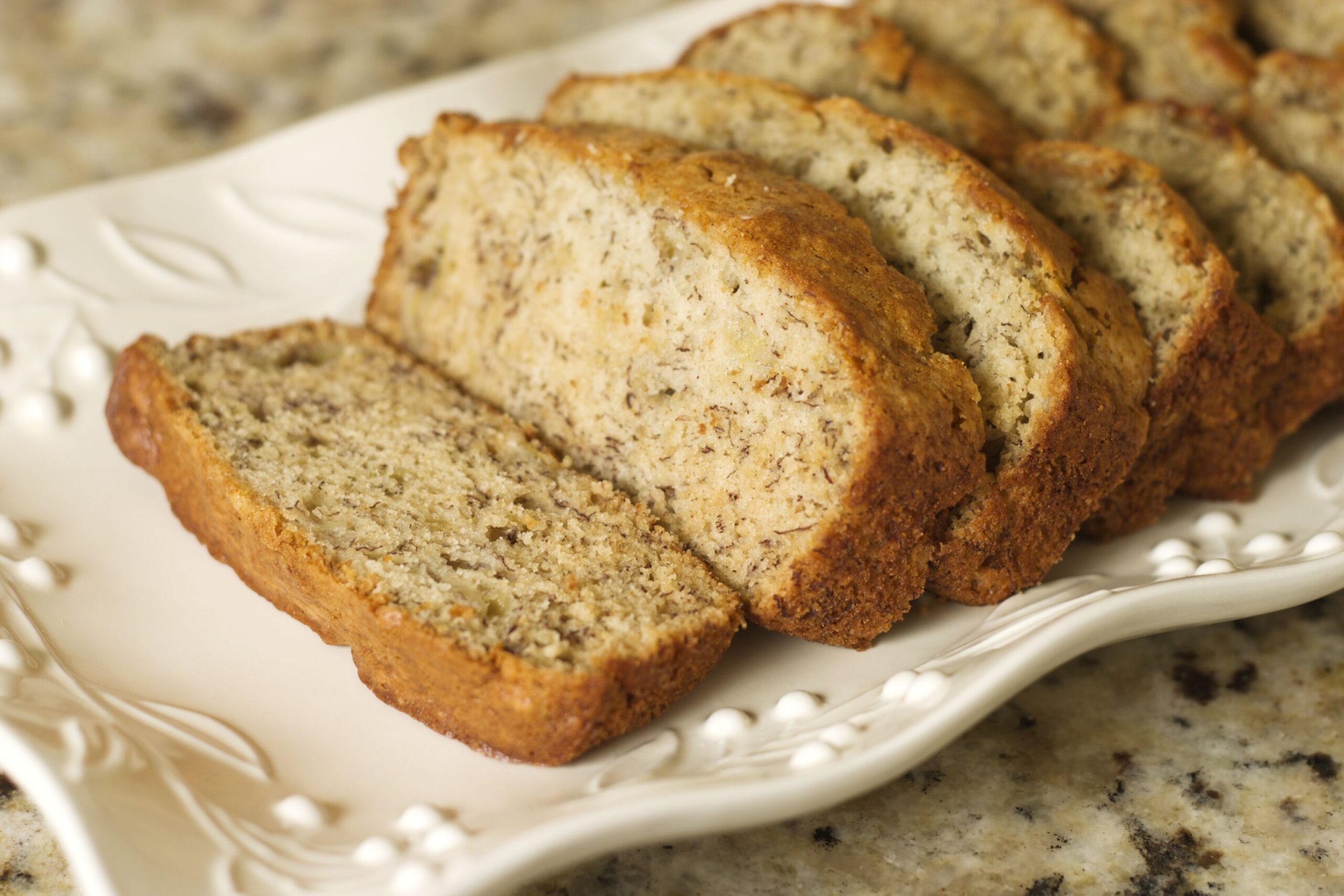 Sliced banana bread on a platter. Shallow DOF. Focus on front end of loaf.
