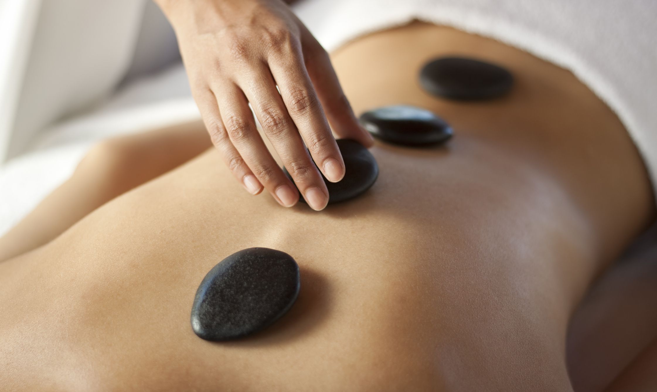 Hands massaging lower back with warm stones. You may also like:
