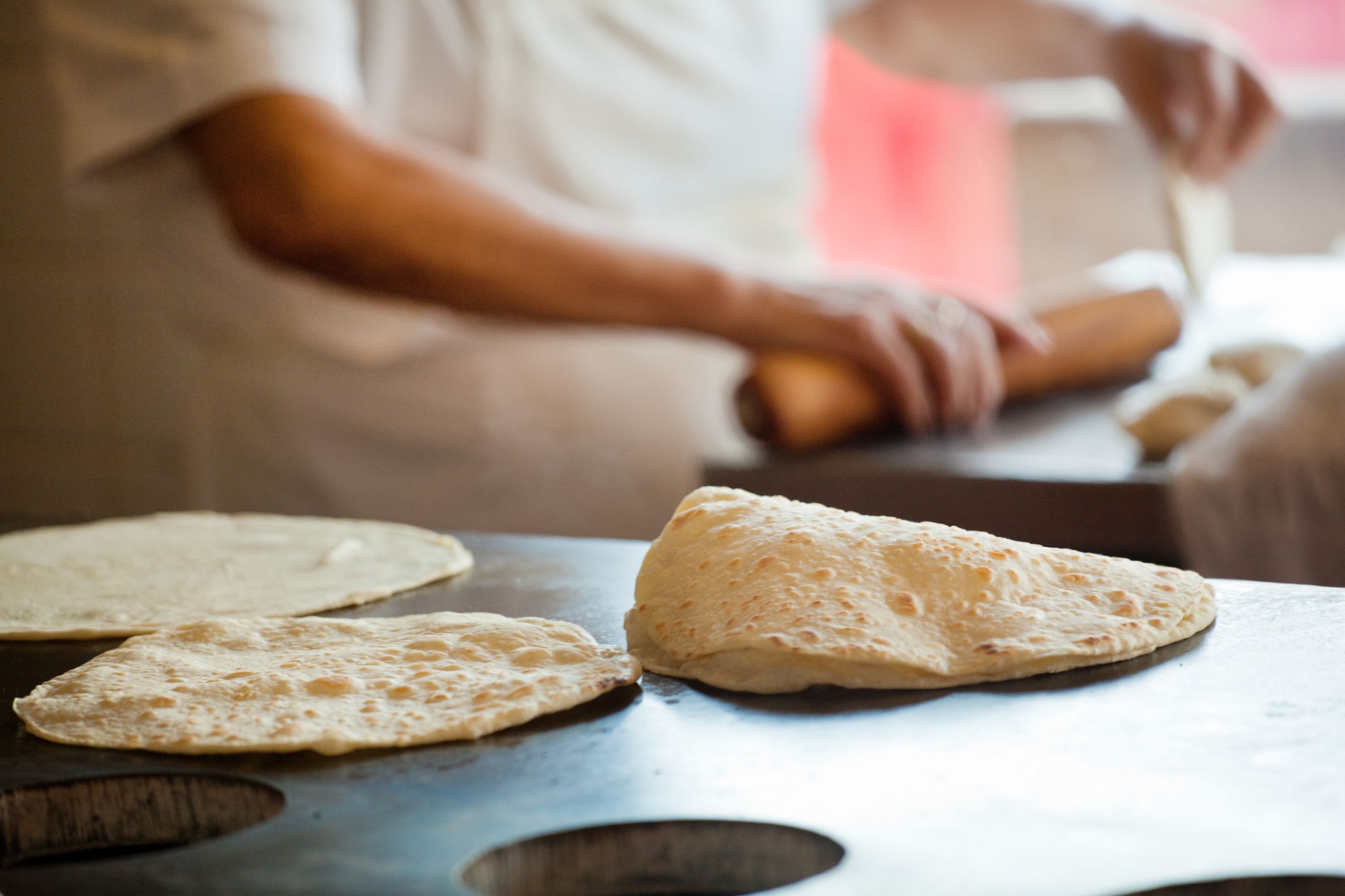 Chef rolling, frying and toasting flour tortillas on a griddle in a Mexican restaurant commercial kitchen.