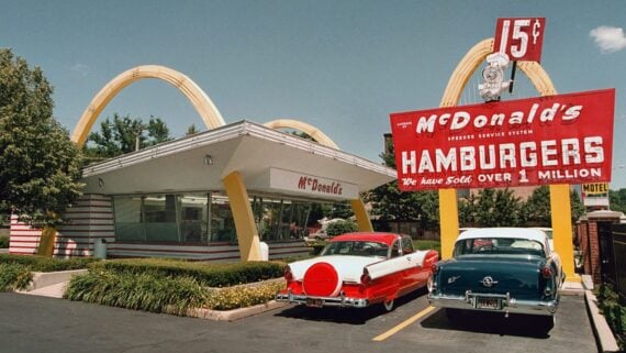 A 1950s-style McDonald's restaurant with golden arches, a retro red sign advertising 15-cent hamburgers, and two classic cars parked in front&mdash;an iconic spot among companies founded by year. The sign states, "We have sold over 1 million.