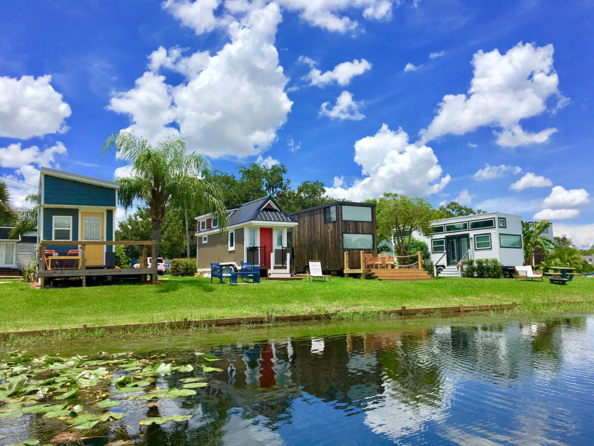 Orlando Lakefront at College Park, Orlando, Florida, lake in the foreground with four tiny homes on shore, reflection of clouds in sky in the lake, many tiny homes in the background