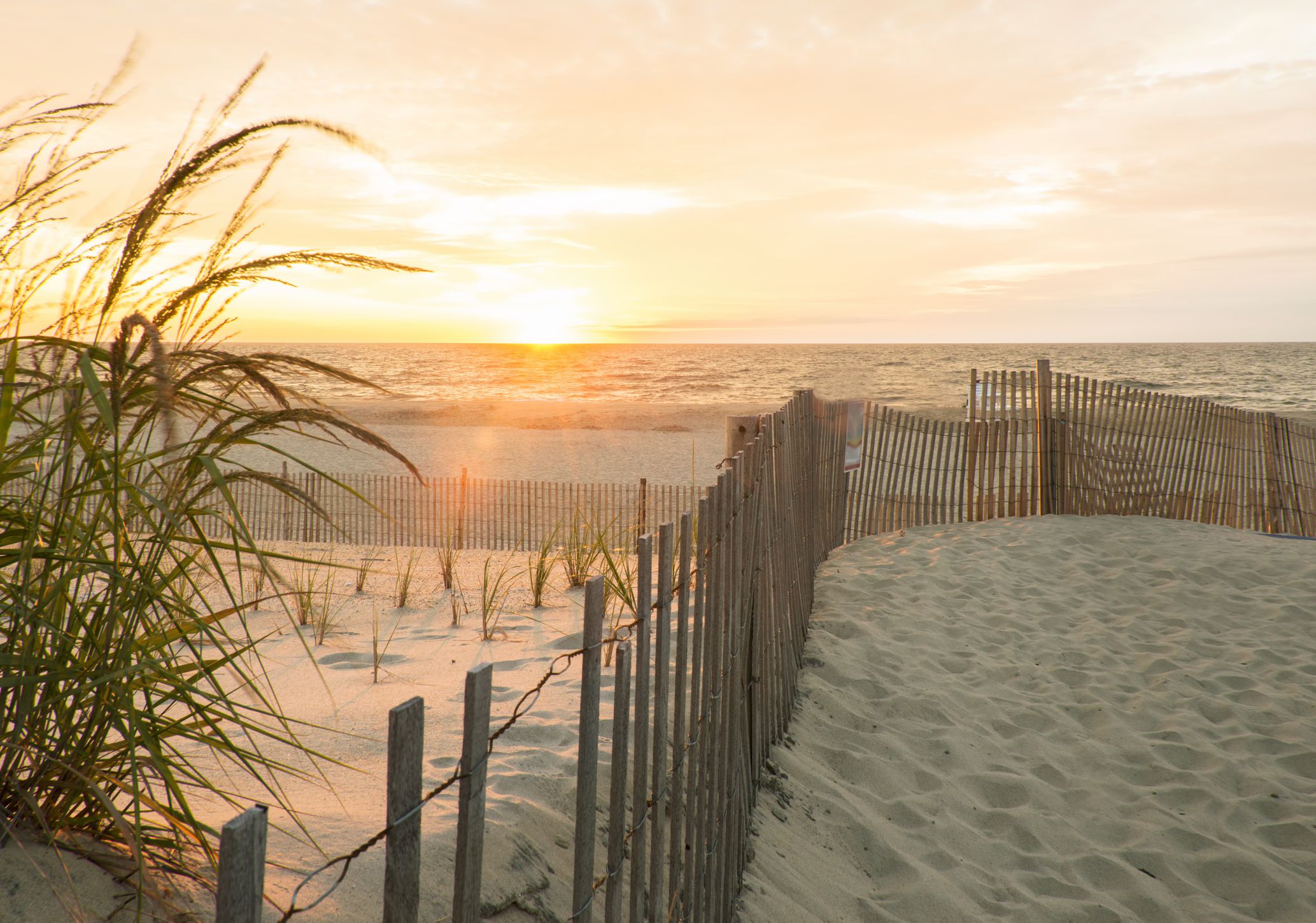 Sunrise at South Bethany Beach, Delaware in Sussex County, rustic fence snaking in the foreground onto beach, ocean and pink sky in the background